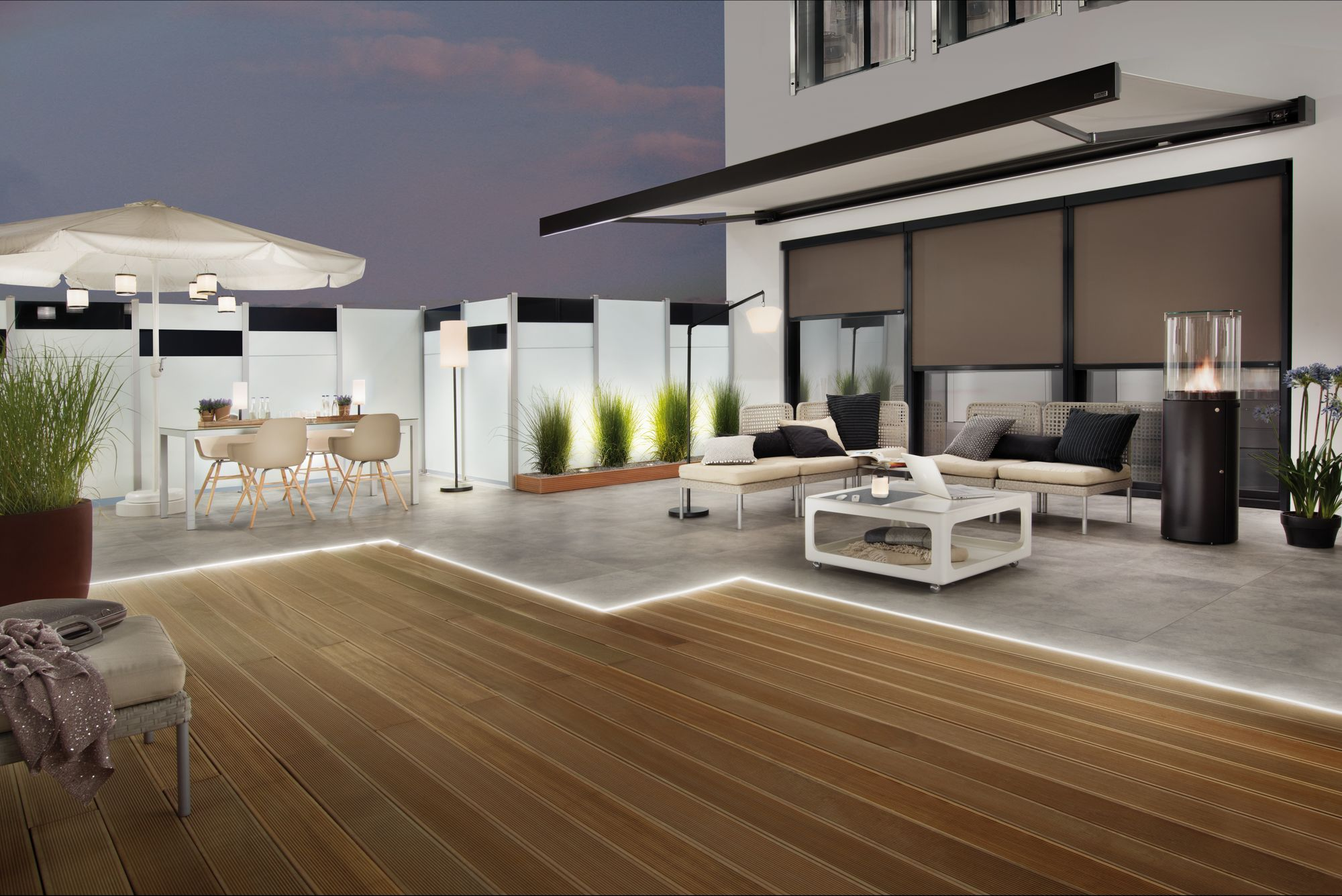 Patio o zmierzchu z tarasem, meblami ogrodowymi i oświetleniem.