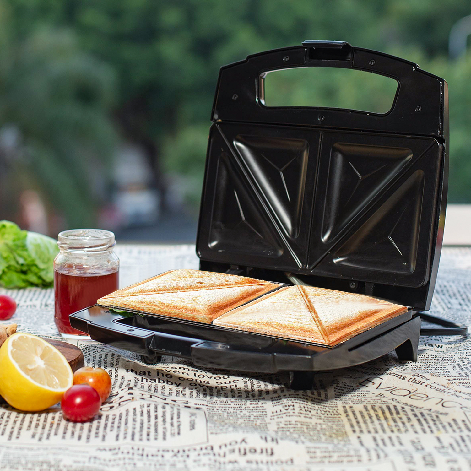 Ein Sandwich-Toaster mit zwei getoasteten Sandwiches. Zusätzliche Zutaten wie Zitrone und Tomaten sind vorhanden.
