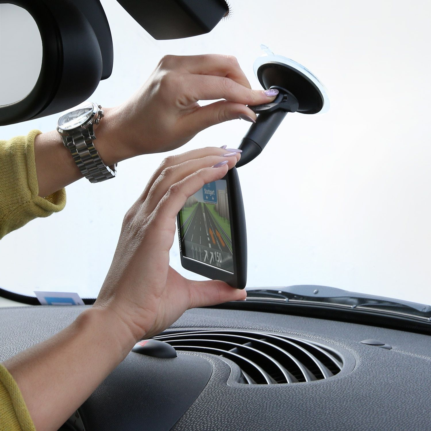 Hände installieren ein GPS-Gerät an der Windschutzscheibe eines Autos. Das Gerät zeigt eine Karte.