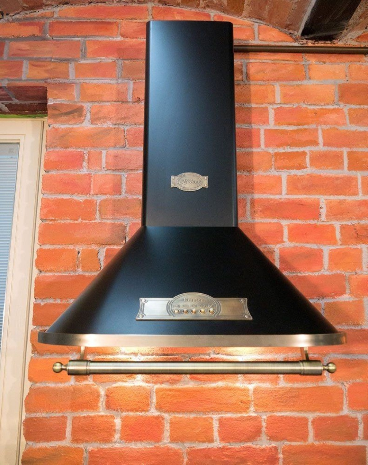 Eine schwarze Dunstabzugshaube vor einer roten Backsteinmauer mit Messingstange und -armaturen.