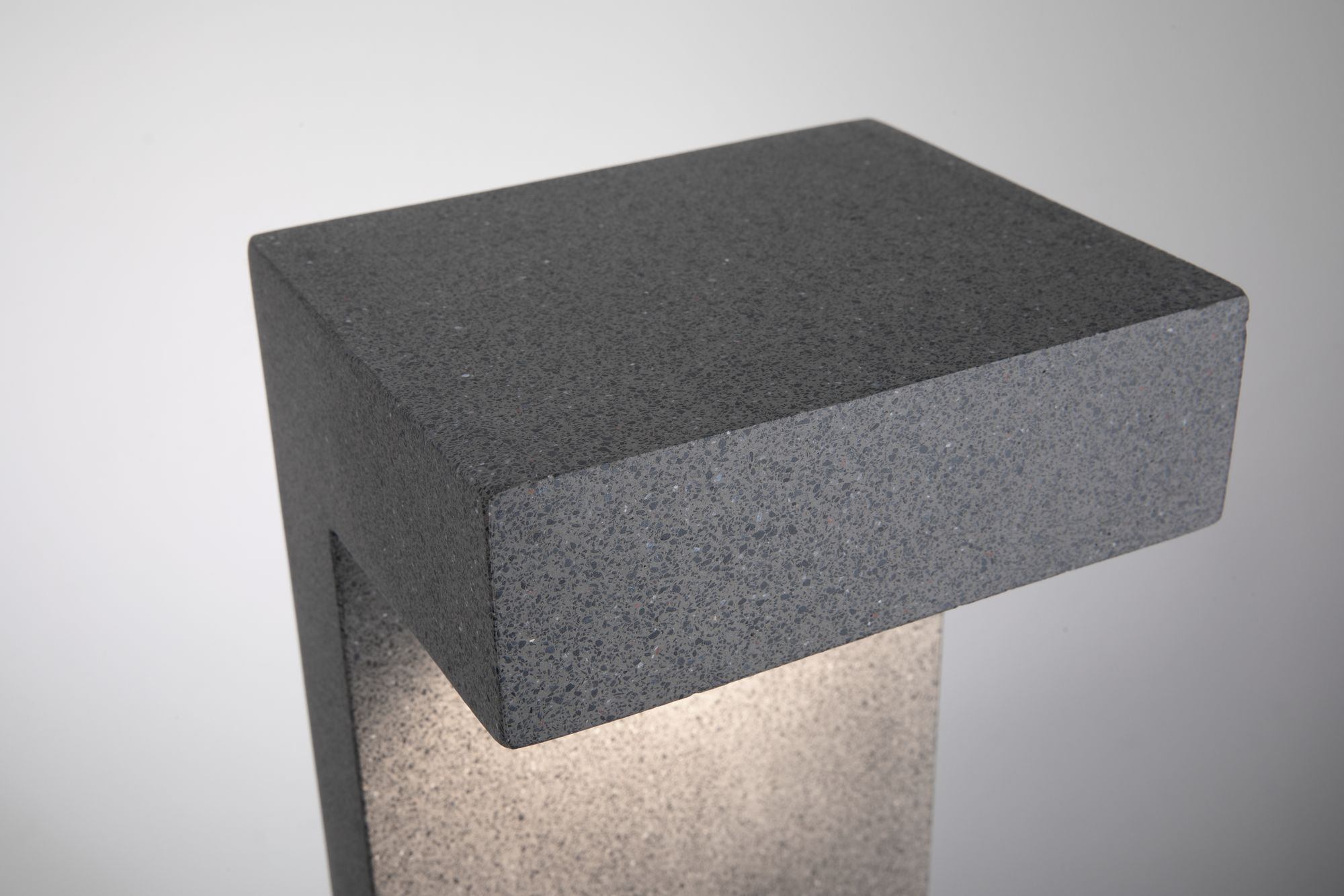 Ciemnoszara, prostokątna lampa zewnętrzna ze światłem świecącym w dół. Tło jest białe.