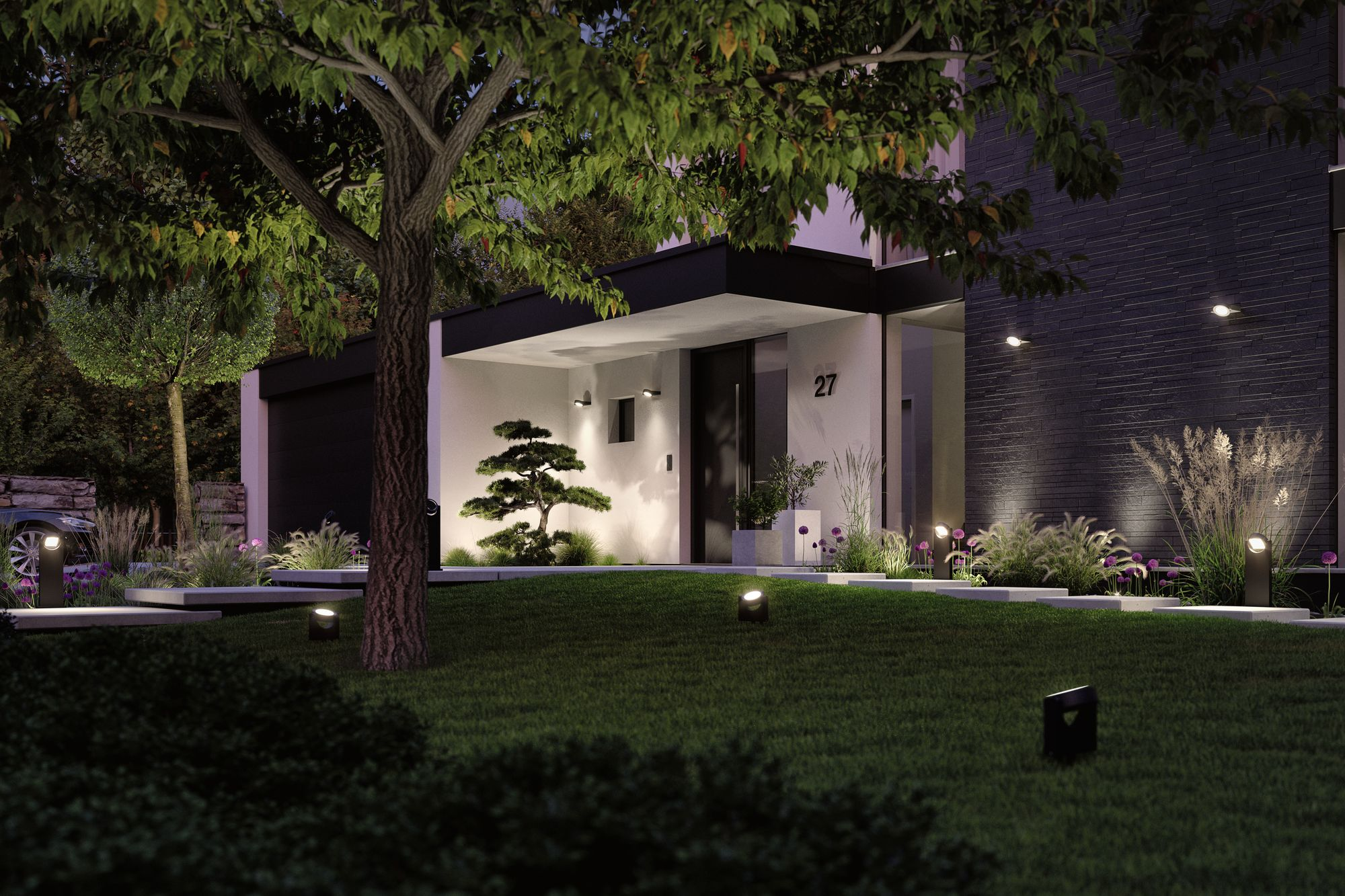 Dom w nocy z oświetleniem trawnika, drzewem i oświetlonym wejściem. Ciemna fasada, numer 27.