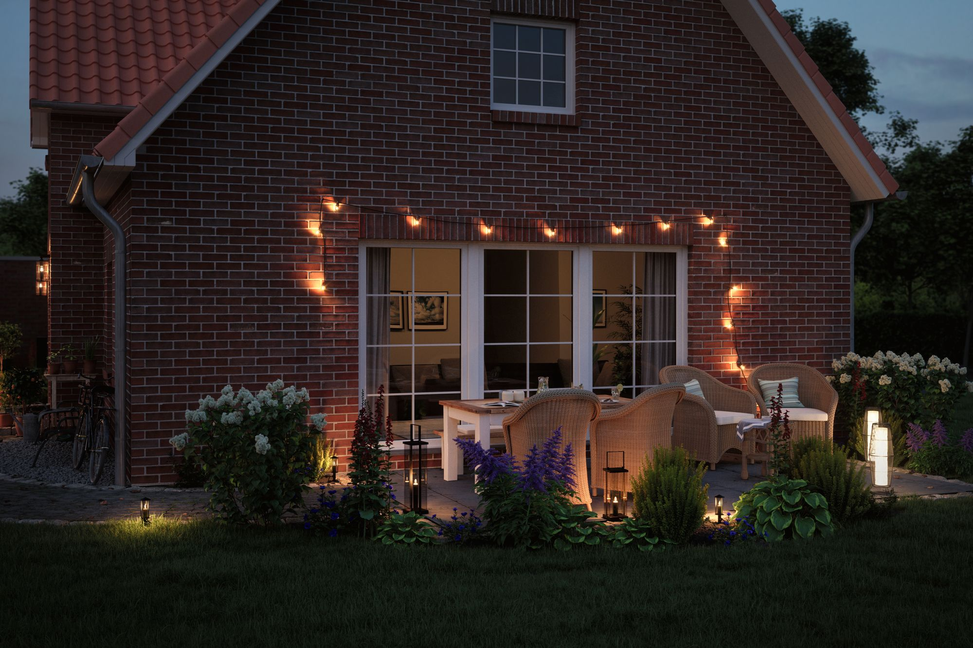 Außenaufnahme eines Hauses in der Dämmerung, mit Lichterketten, Terrassenmöbeln und Gartenleuchten.