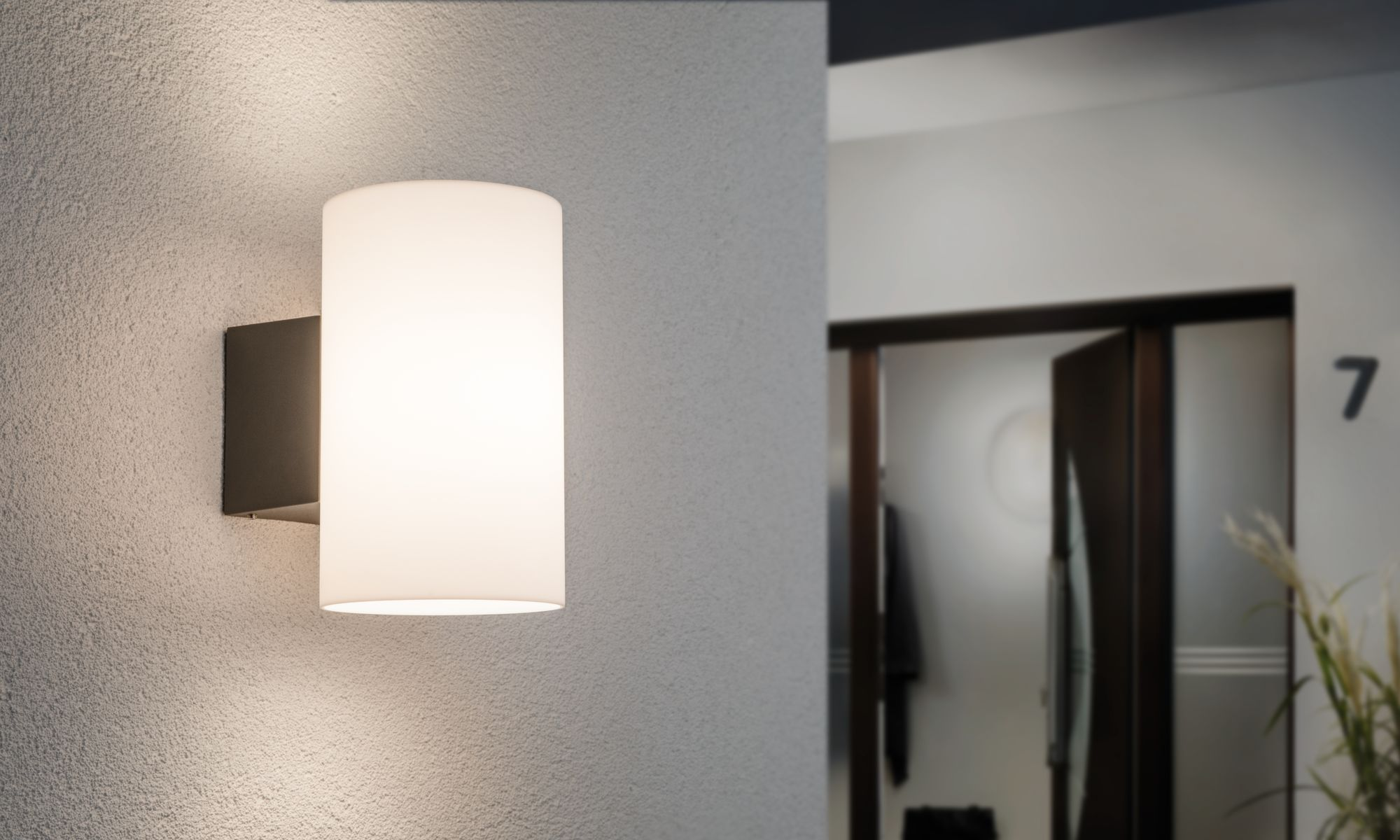 Cylindryczna lampa ścienna z białym kloszem, zamontowana na jasnej ścianie.