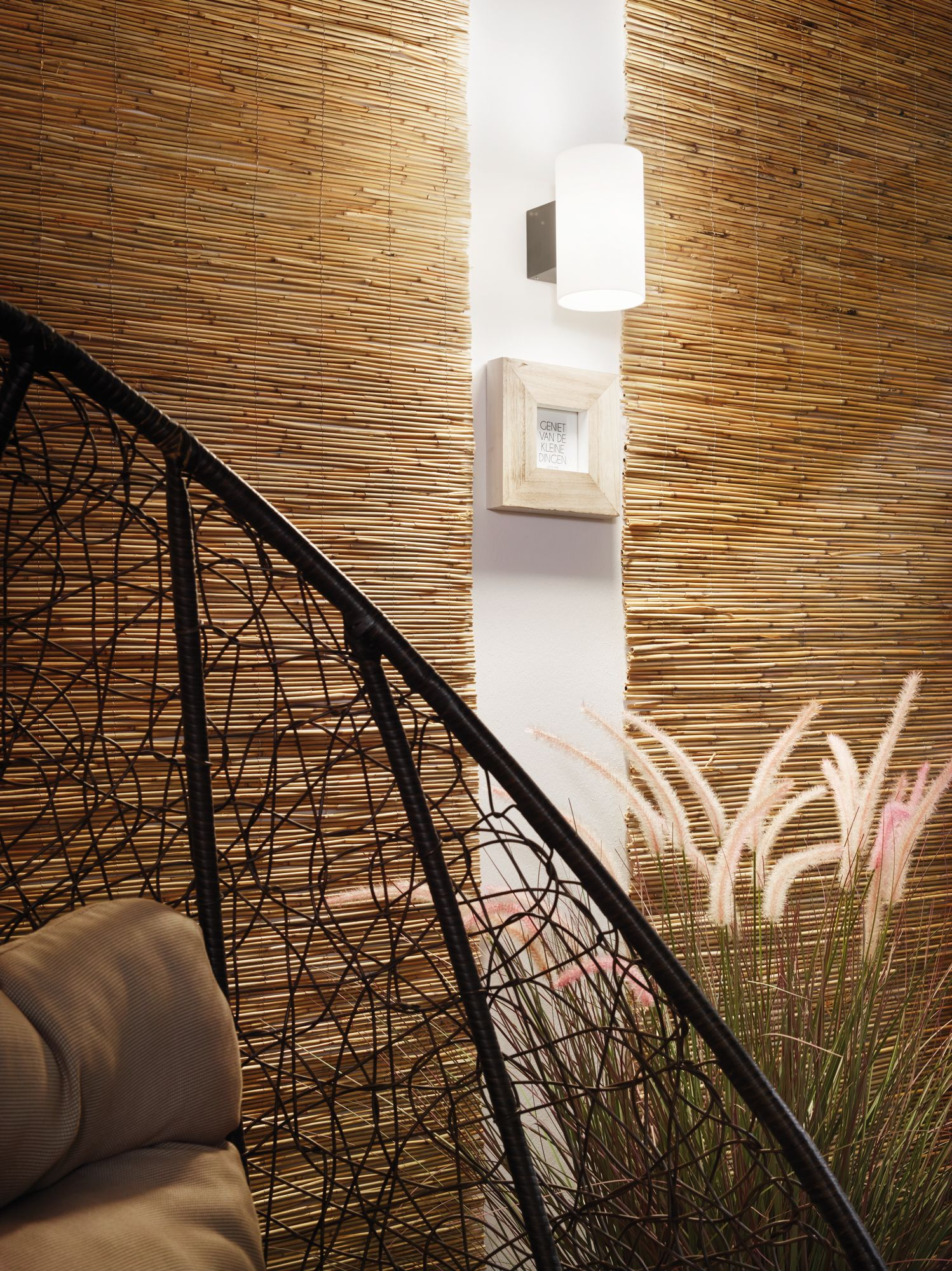 Ujęcie wnętrza przedstawia bambusową ścianę, krzesło, oprawiony obraz i dekoracyjne rośliny z oprawą oświetleniową.