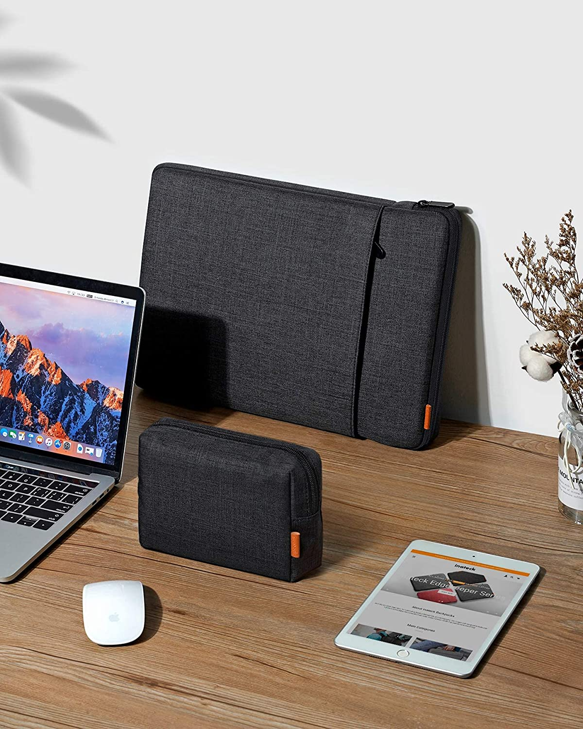 Laptop, Maus und zwei Hüllen auf einem Holztisch, mit Tablet, das eine Website zeigt.