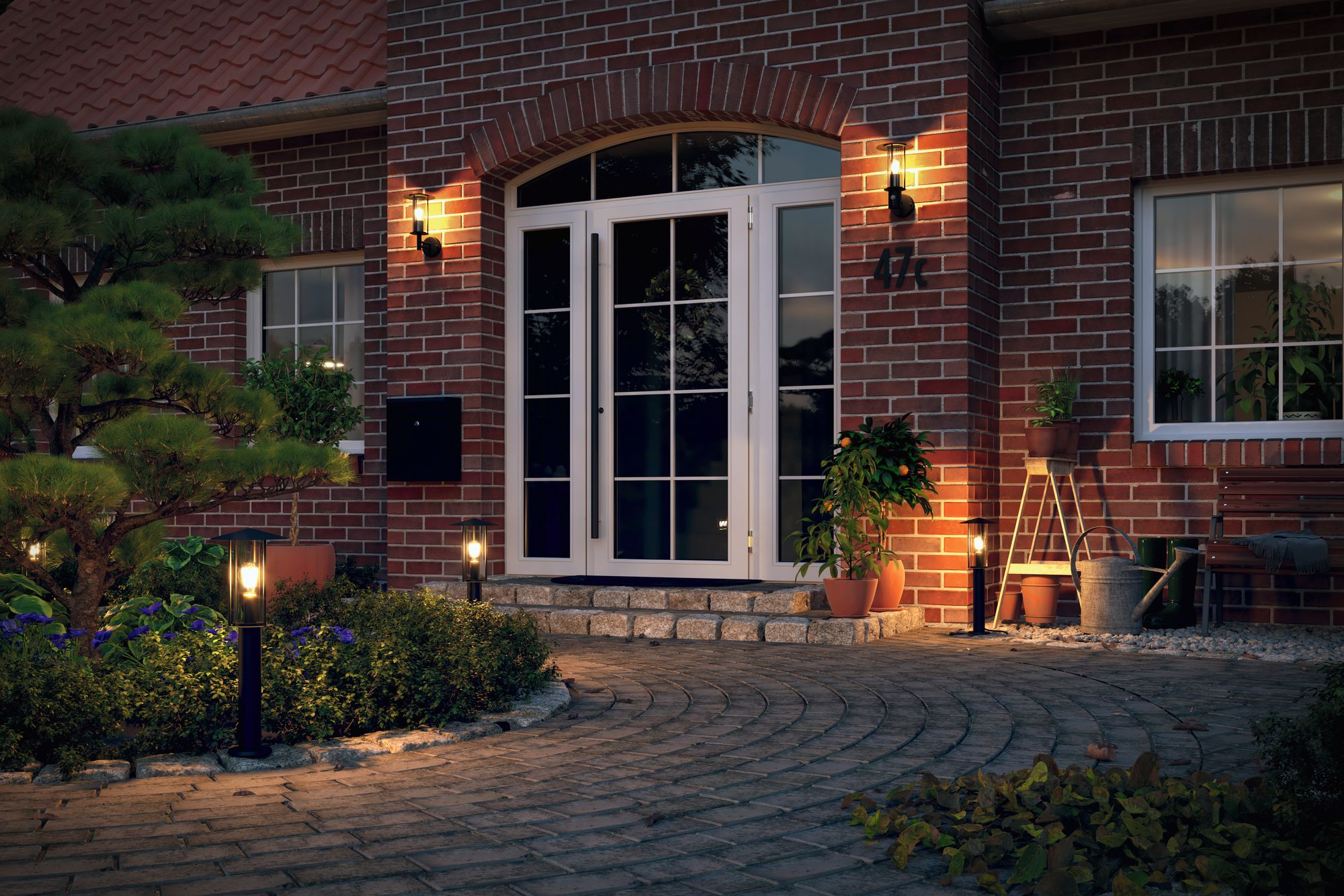 Wejście do domu o zmierzchu, z włączonymi światłami, ceglaną fasadą i kamienną ścieżką.