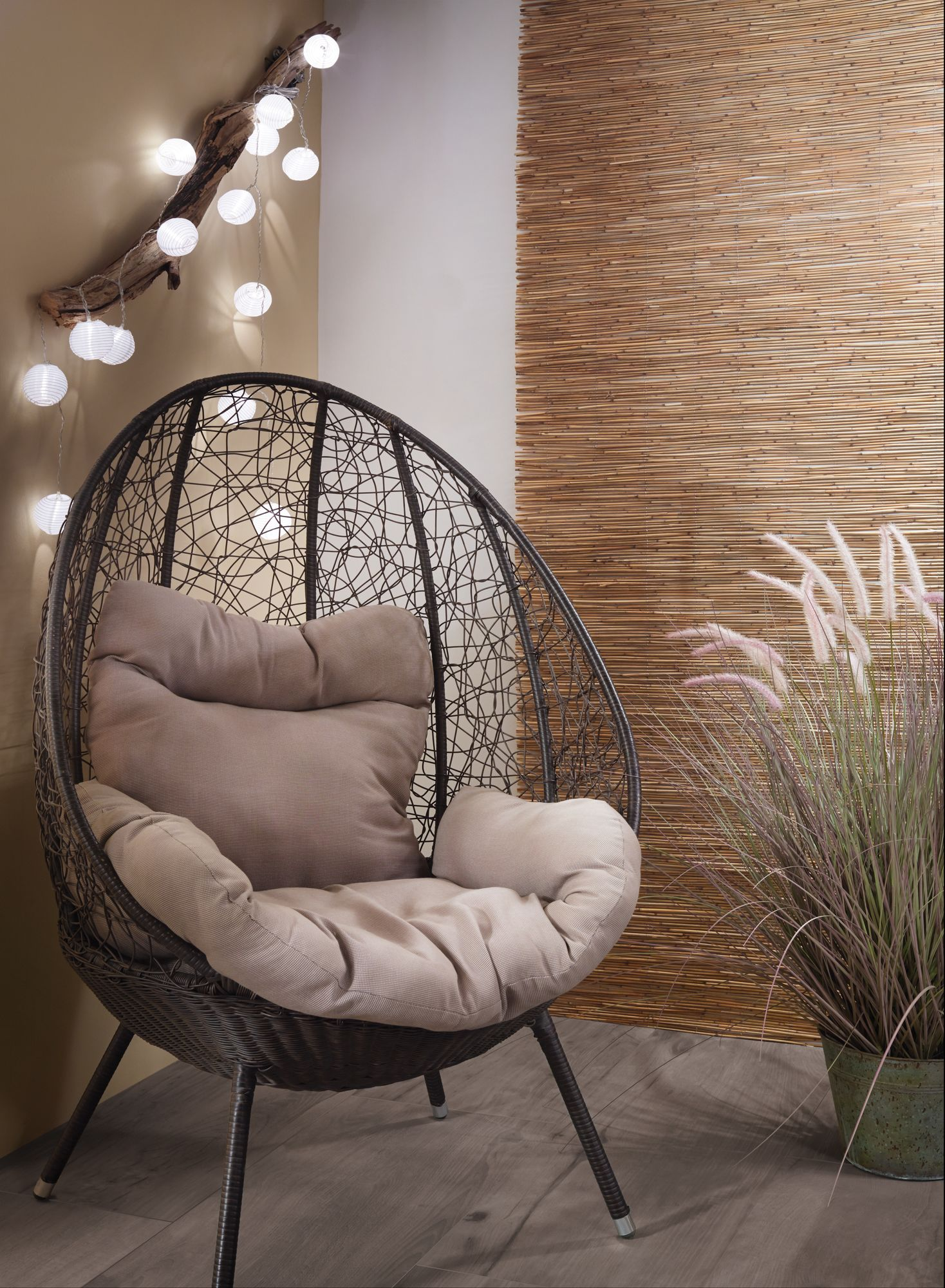 Fotel jajko z poduszką i kocem, z dekoracyjnymi światłami i bambusową ścianą.