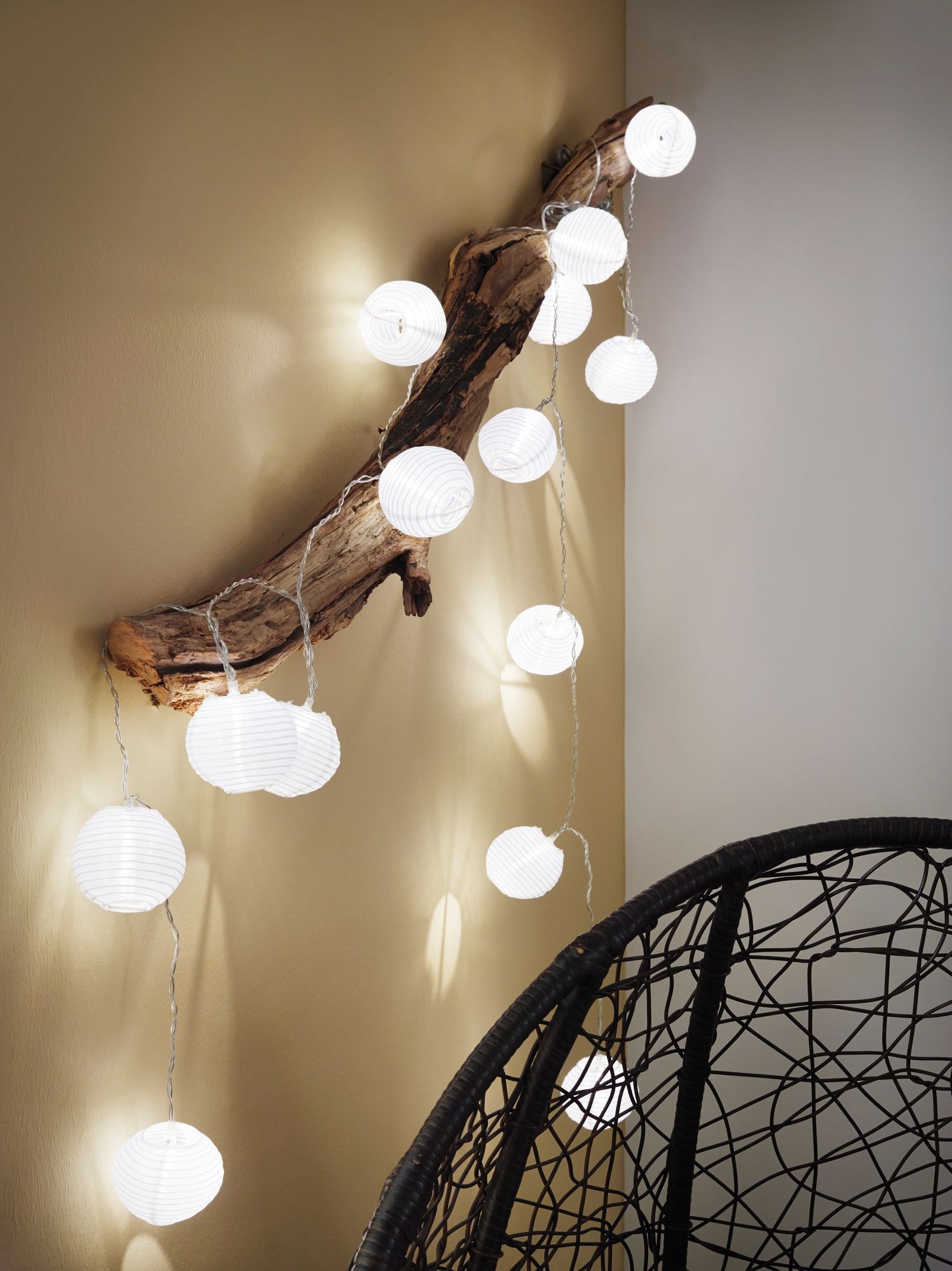 Światła sznurkowe wiszące na gałęzi. Krzesło jest po prawej stronie na dole. Ściana jest beżowa.