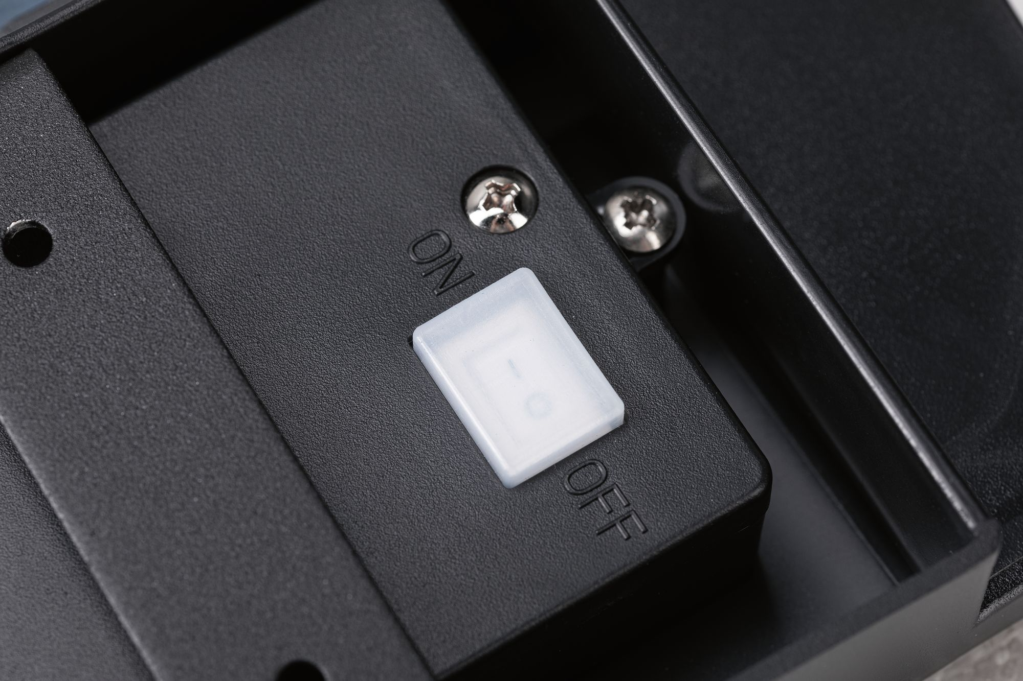 Zbliżenie włącznika/wyłącznika na czarnym urządzeniu. Biały przełącznik z etykietami ON/OFF.