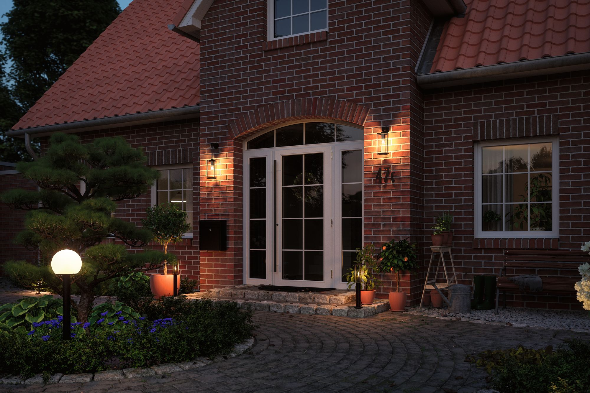 Dom z cegły w nocy. Światła oświetlają drzwi wejściowe i otaczające rośliny.