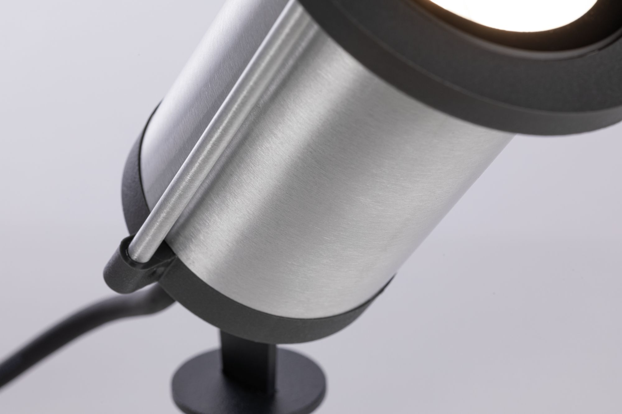 Zbliżenie srebrnego reflektora. Ma czarny pierścień i czarną podstawę. Tło jest białe.