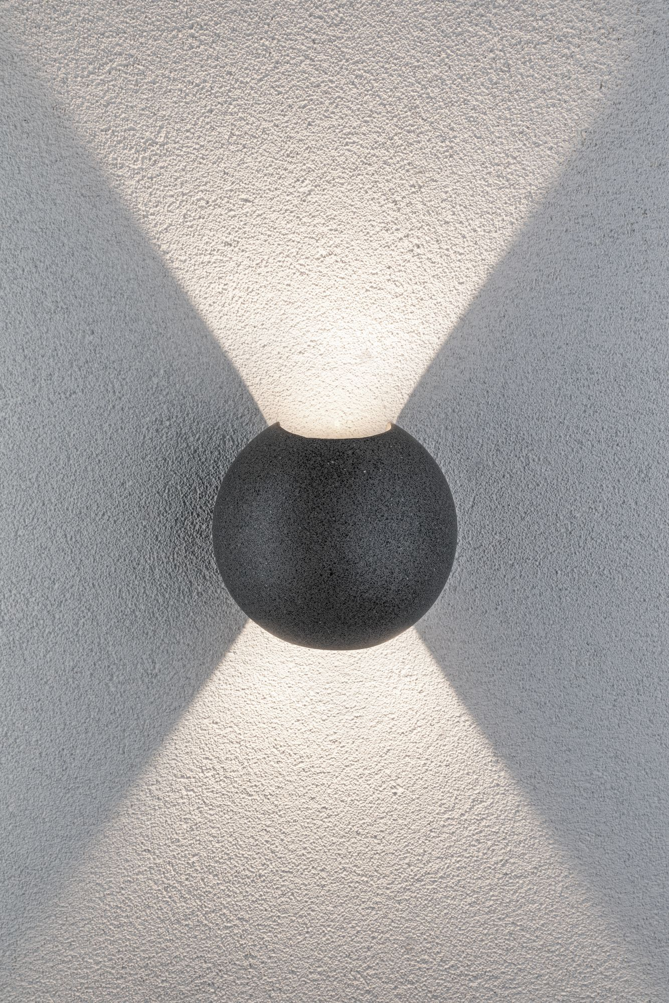 Dunkelgraue kugelförmige Lampe an strukturierter weißer Wand mit Lichtstrahlen.