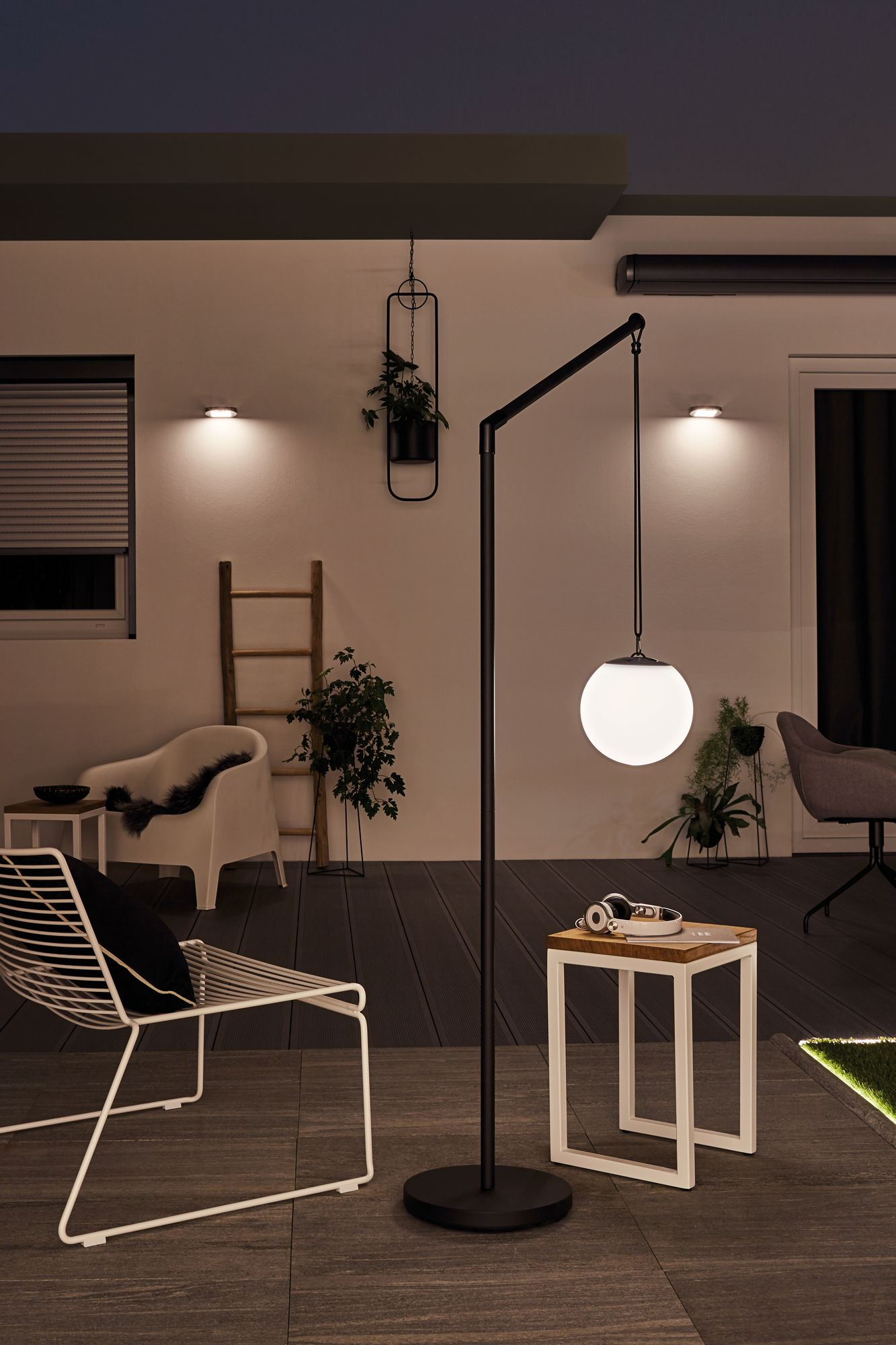 Scena na zewnątrz w nocy. Wysoka lampa z okrągłym światłem. Meble obejmują krzesło, stolik i drabinę.