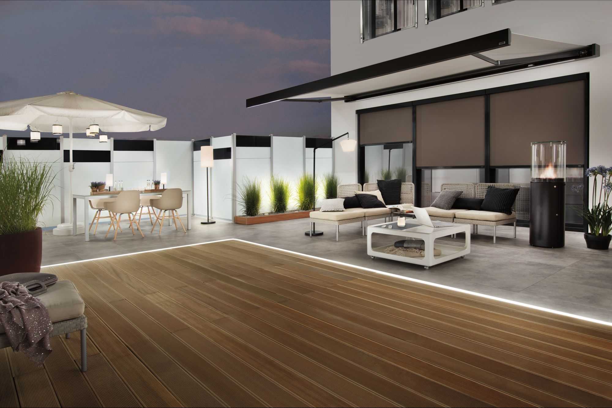 Terrassenszene: Holzterrasse, weiße Möbel, hohe Pflanzen und eine moderne Feuerstelle.