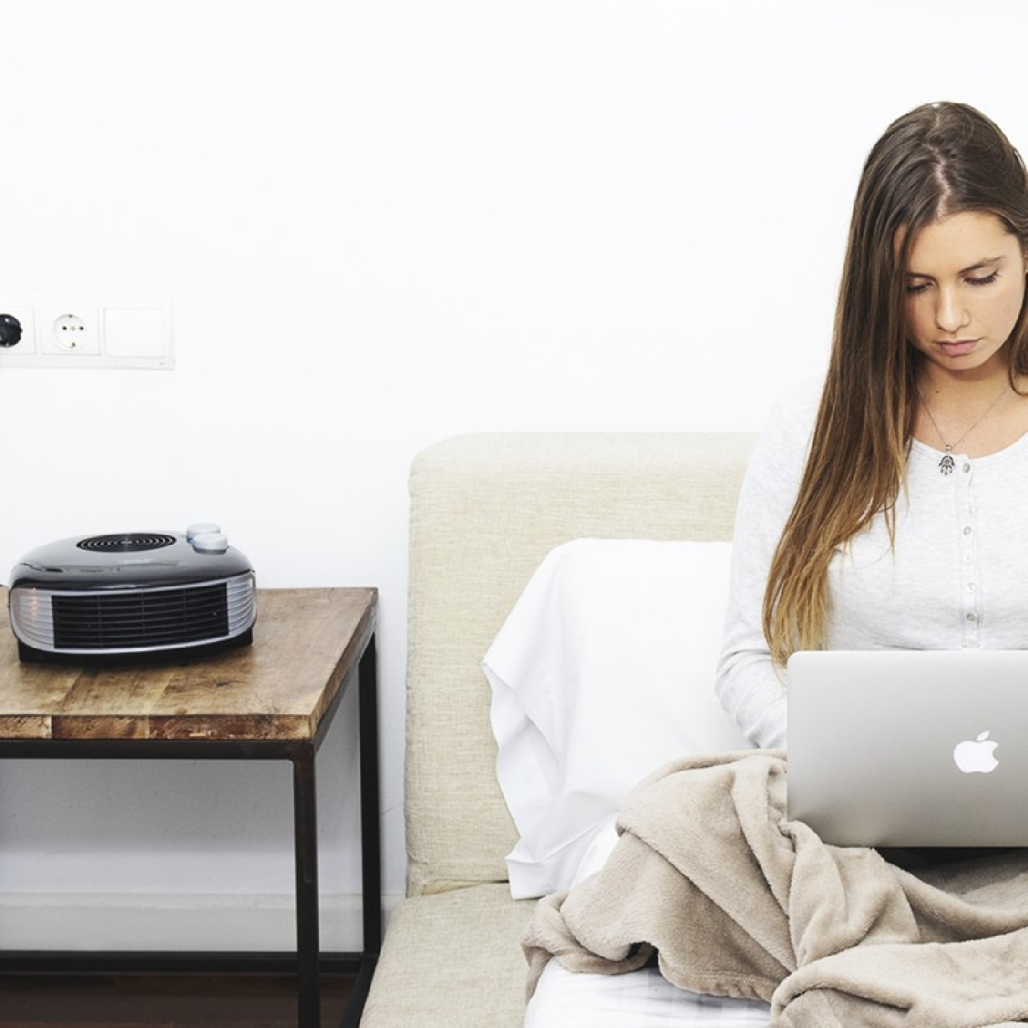 Vrouw die laptop gebruikt op bed. Een kachel en een bijzettafel op de achtergrond.
