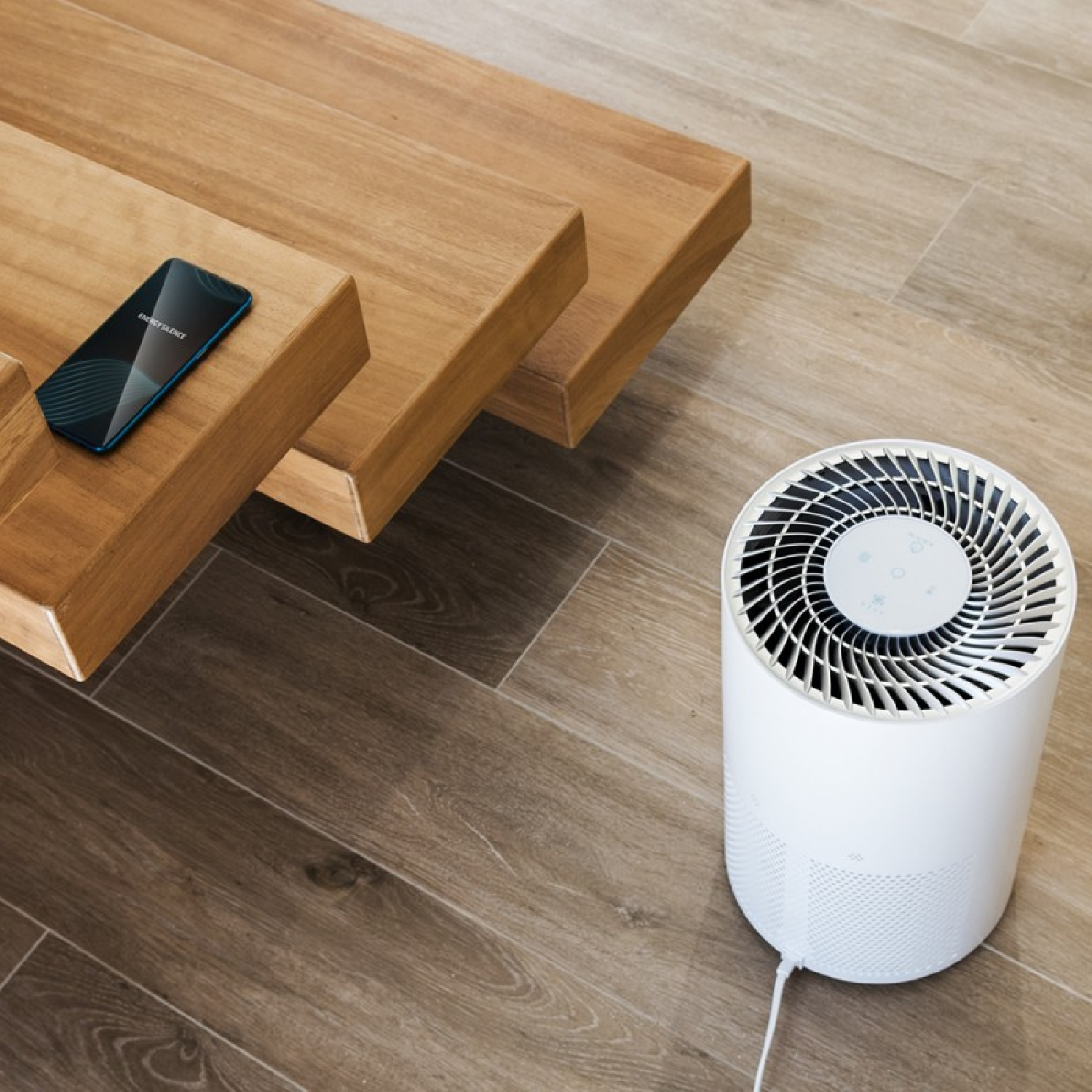 Un purificatore d'aria bianco accanto a un tavolo di legno e un telefono.