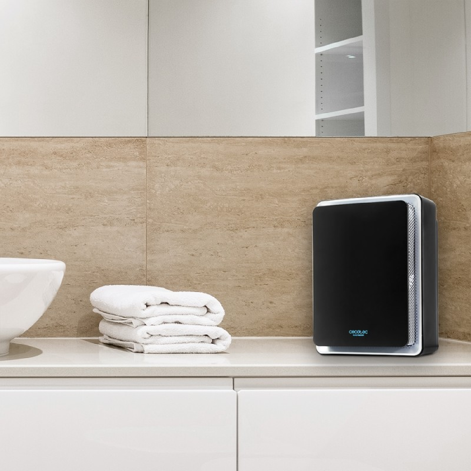 Czarny oczyszczacz powietrza stoi na blacie. Obok złożone są białe ręczniki.