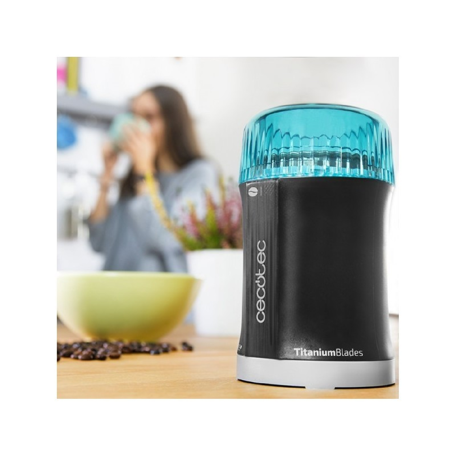 Schwarz-silberne Kaffeemühle mit blauem Deckel. Frau trinkt im Hintergrund Kaffee.