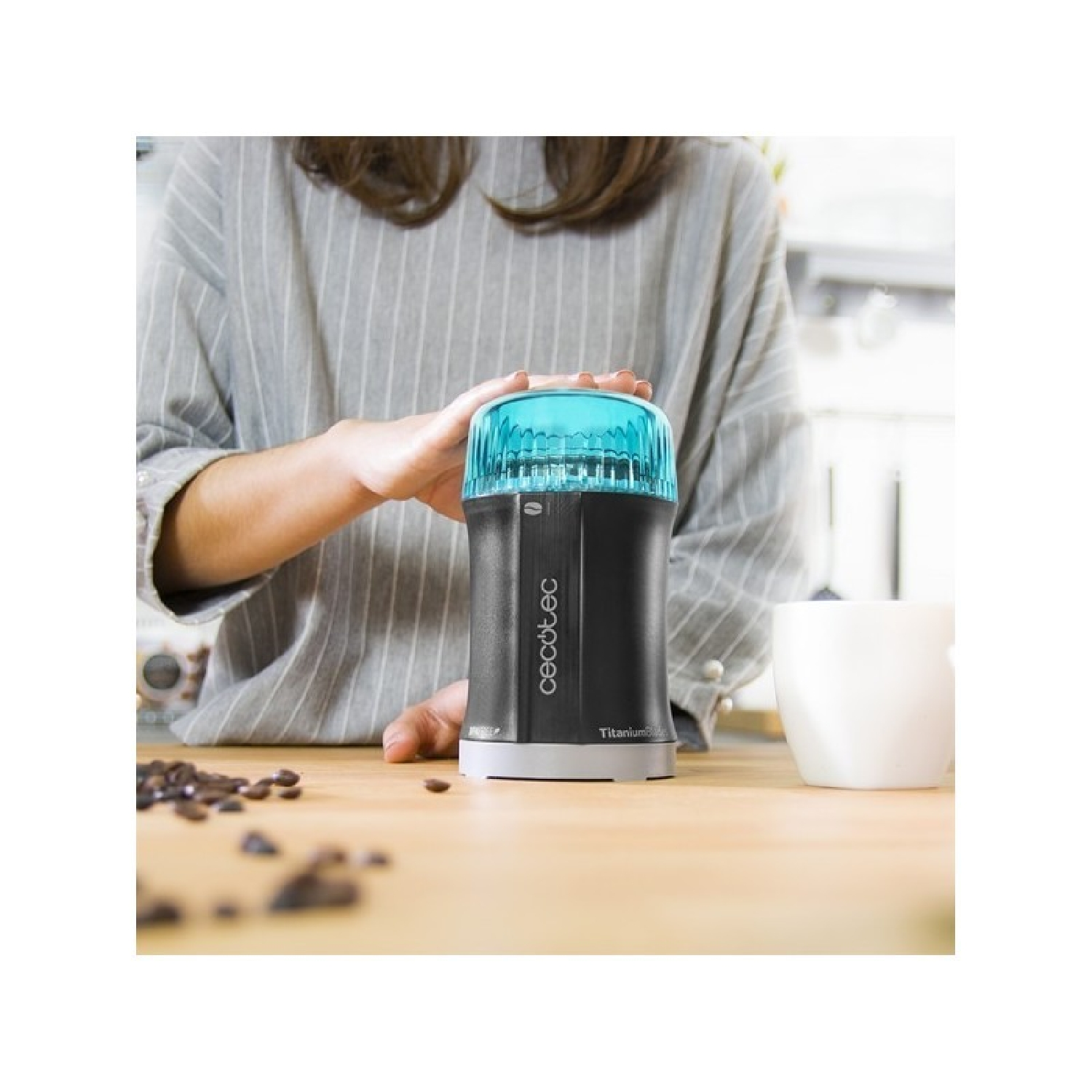 Hände halten eine schwarze und teal Kaffeemühle, mit Kaffeebohnen und einer weißen Tasse.
