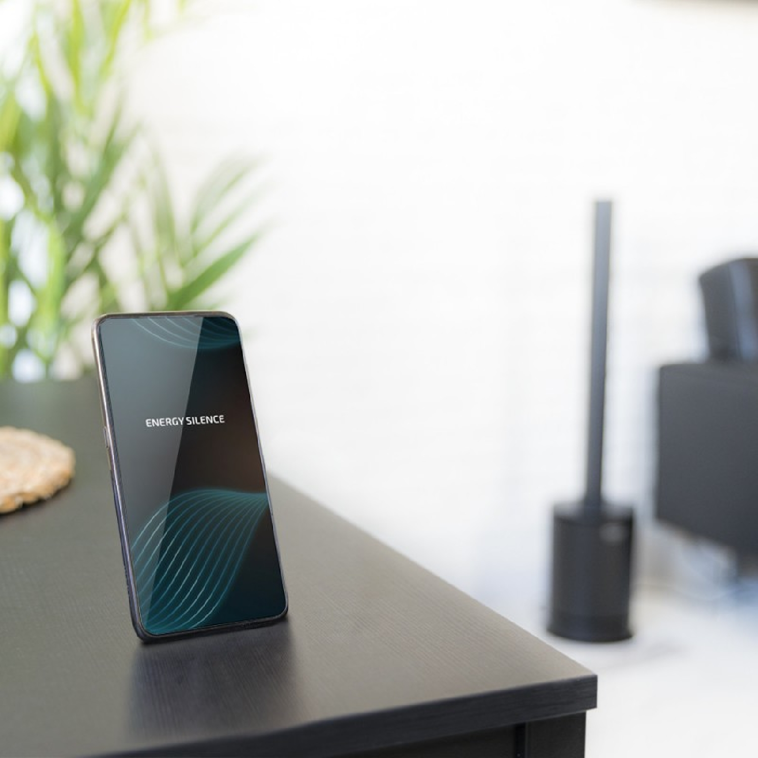 Uno smartphone su un tavolo scuro, che mostra 'ENERGY SILENCE' sullo schermo e un ventilatore nero sullo sfondo.