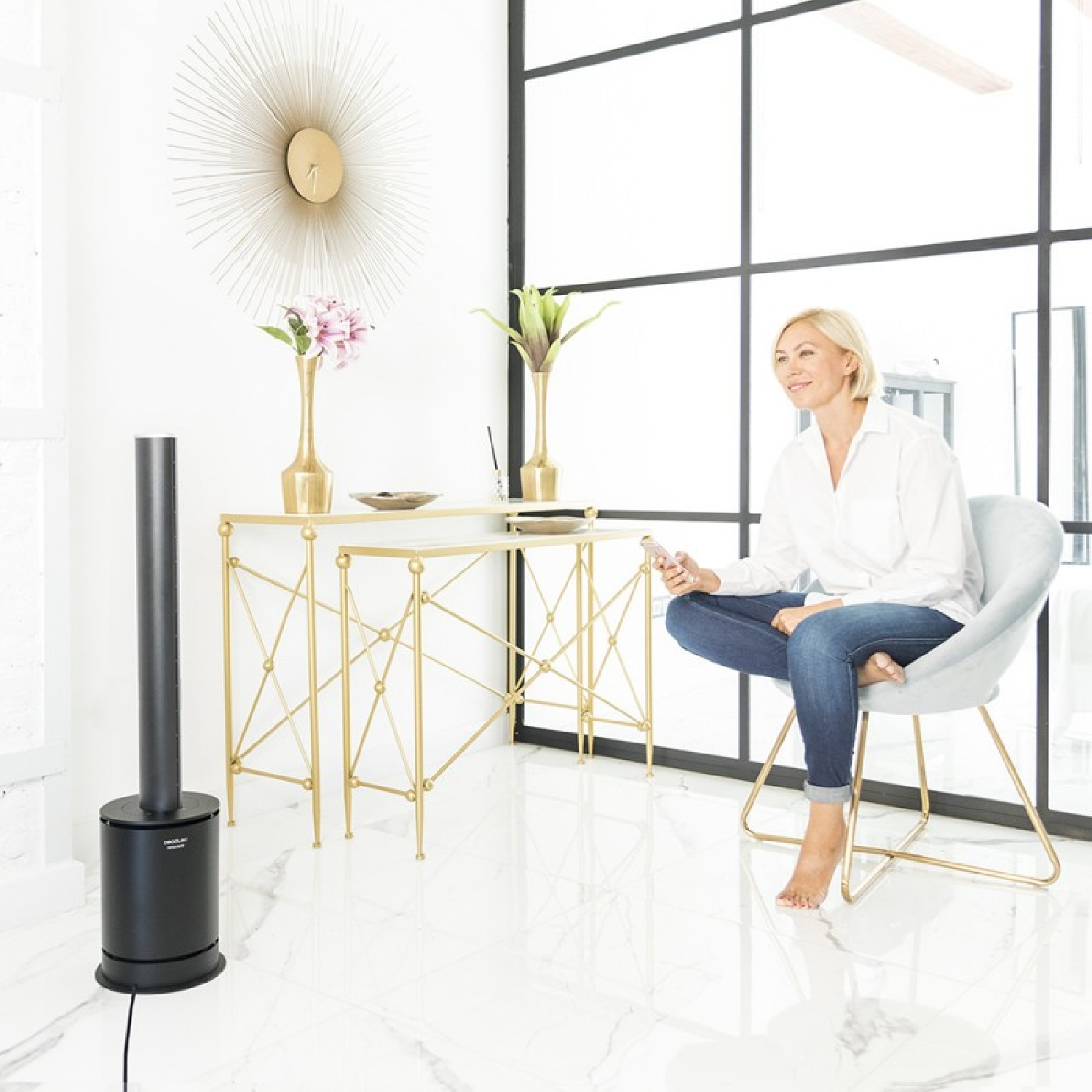 Una donna in una stanza, seduta su una sedia, che tiene un telecomando, con un ventilatore e decorazioni.