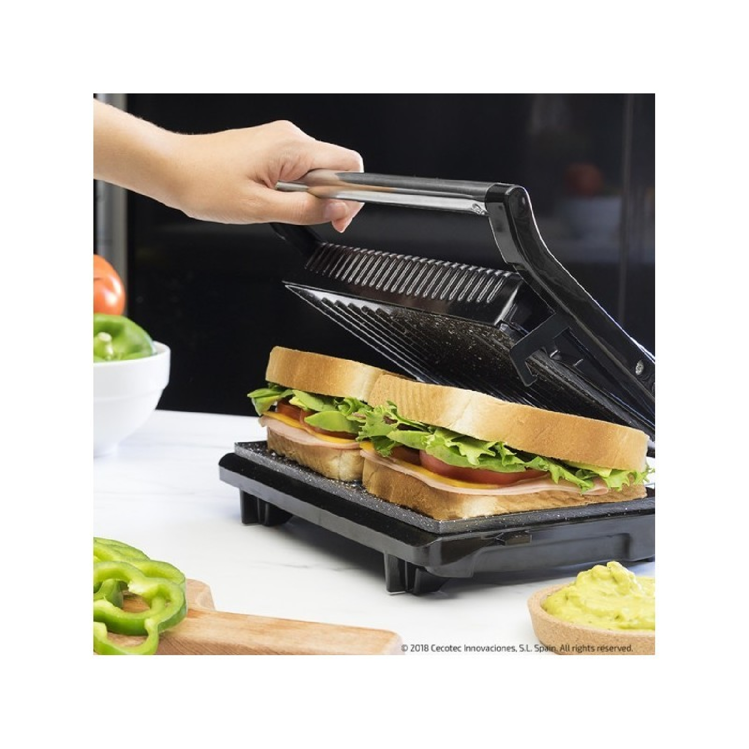 Kanapki na czarnym grillu. Ręka trzymająca uchwyt. Zielona papryka i guacamole.