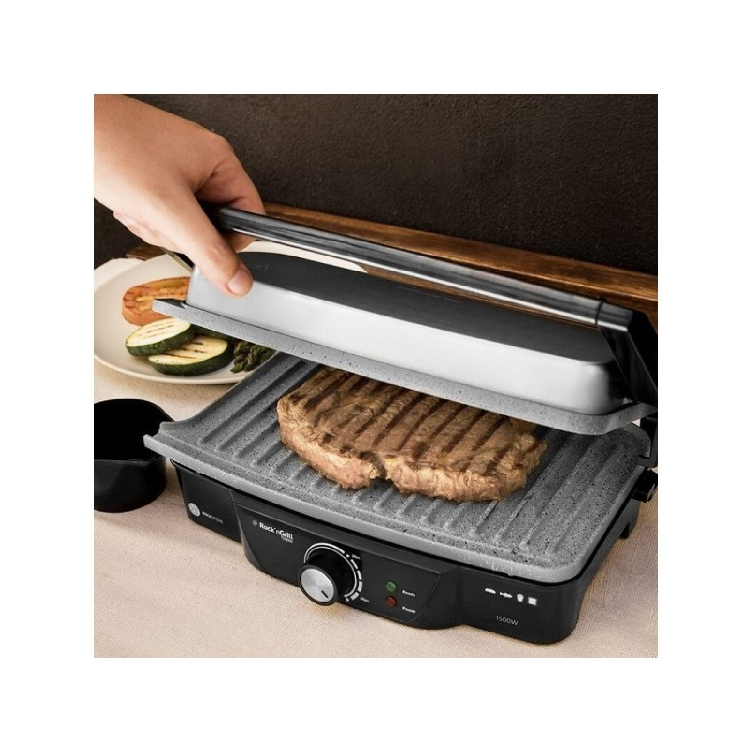 Ręka osoby opuszcza pokrywę grilla. Na grillu jest stek.