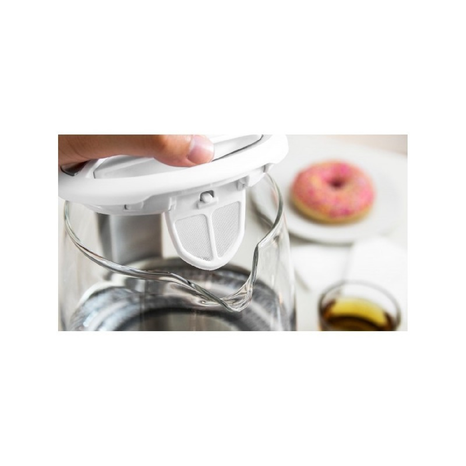 Eine Hand hält den Deckel eines Glaskessels. Donut und Tee im Hintergrund.
