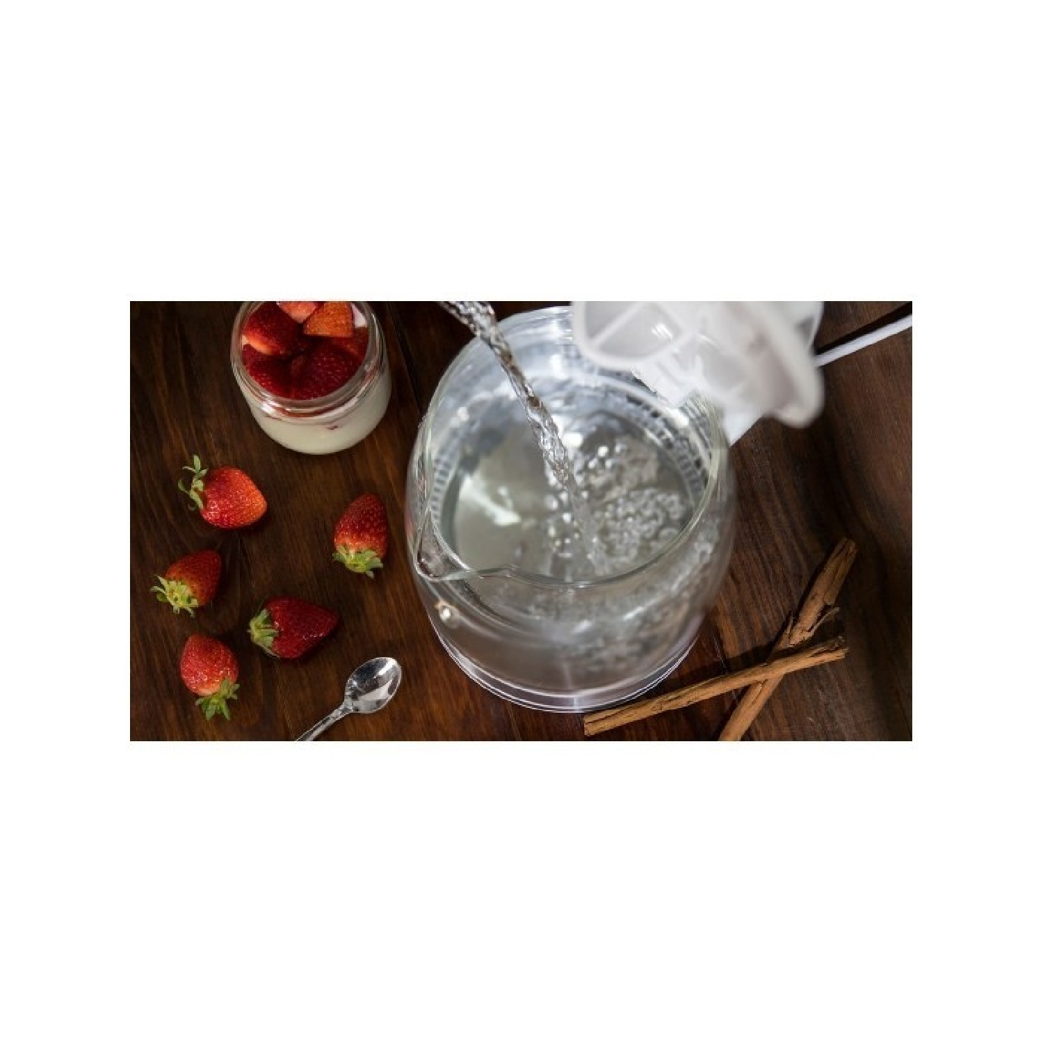 Wasser gießt in einen Glaskrug mit Erdbeeren und Zimtstangen. Holztisch.