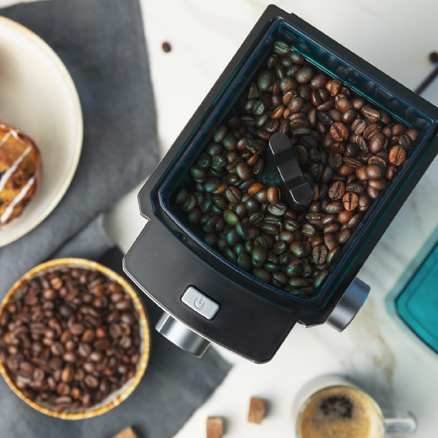 Widok z góry na młynek do kawy z ziarnami kawy i innymi przedmiotami związanymi z kawą.