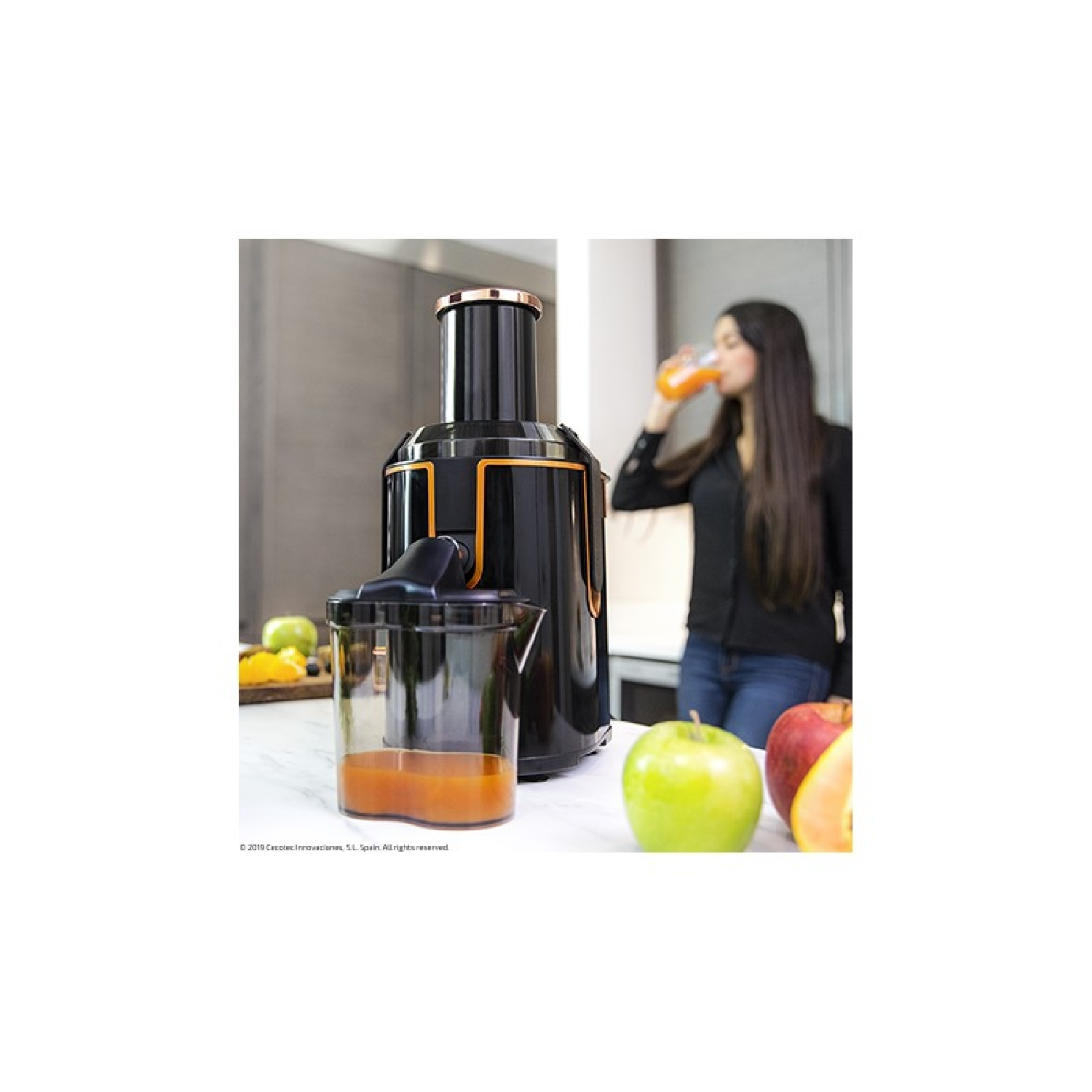 Donna che beve succo vicino a un estrattore. Mele e altri frutti su una superficie bianca.