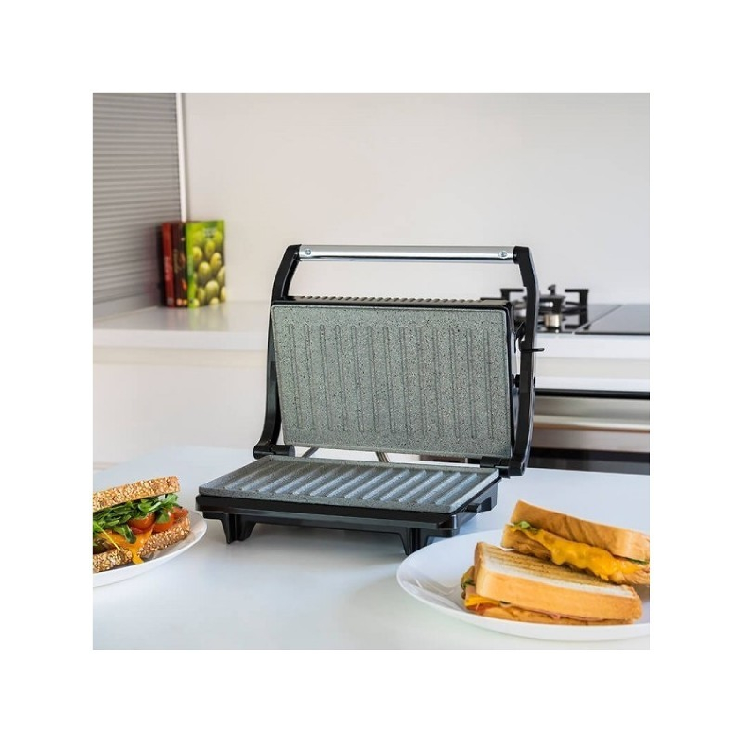 Otwarta prasa do panini na białym stole z kanapkami, wnętrze kuchni w tle.