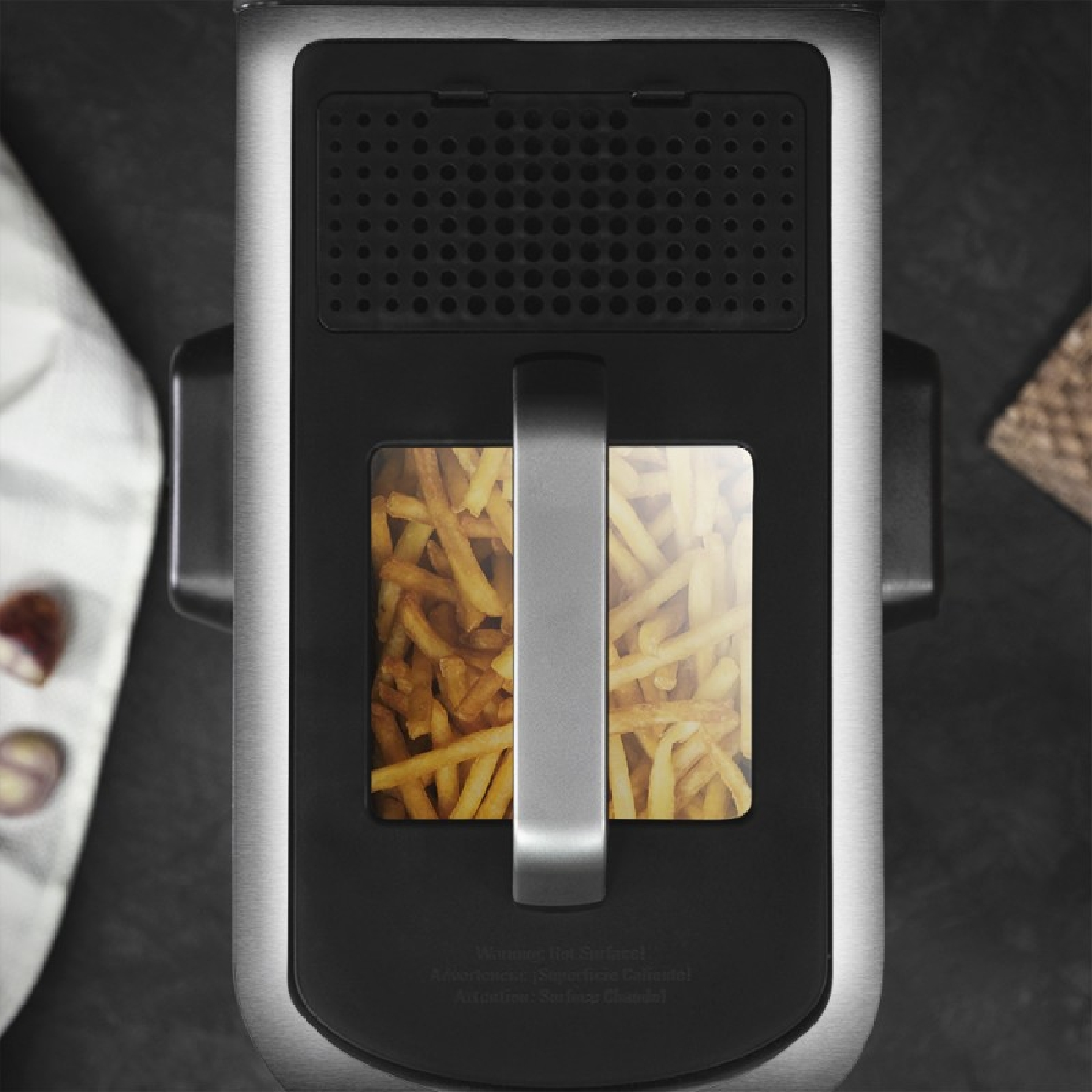 Widok z góry na frytownicę, wypełnioną złotymi frytkami. Urządzenie jest czarne i srebrne.