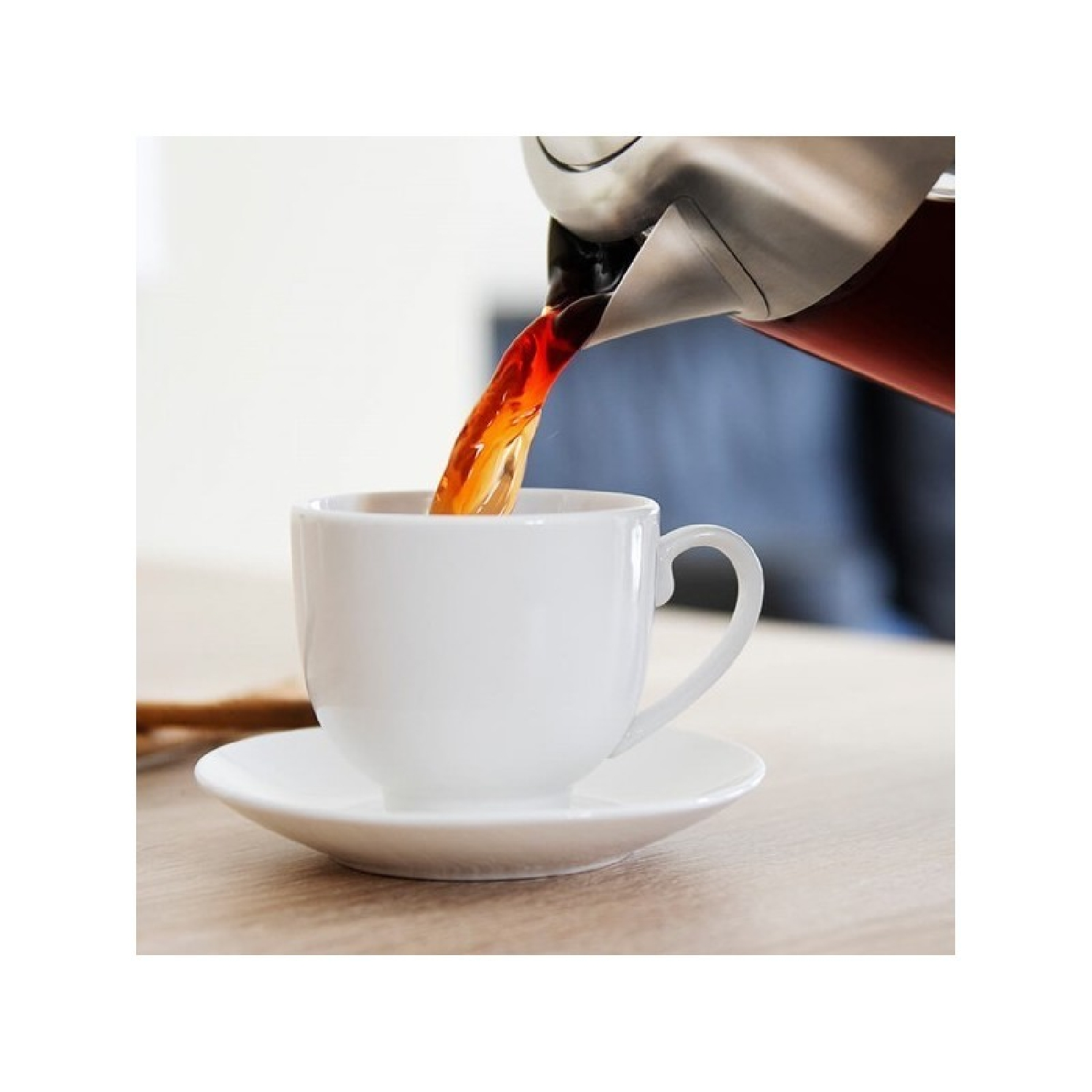 Eine weiße Tasse und Untertasse, die mit dunkler Flüssigkeit aus einem silbernen Topf gefüllt werden.
