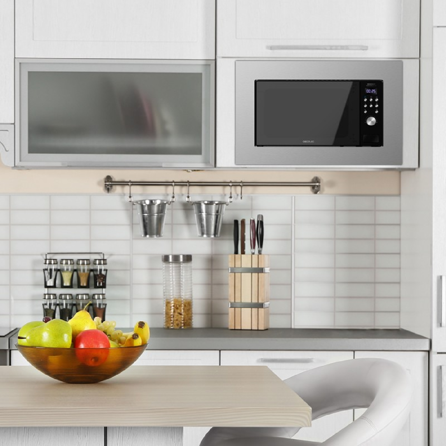 Kuchnia z kuchenką mikrofalową, misą z owocami, nożami i wiszącymi wiaderkami.