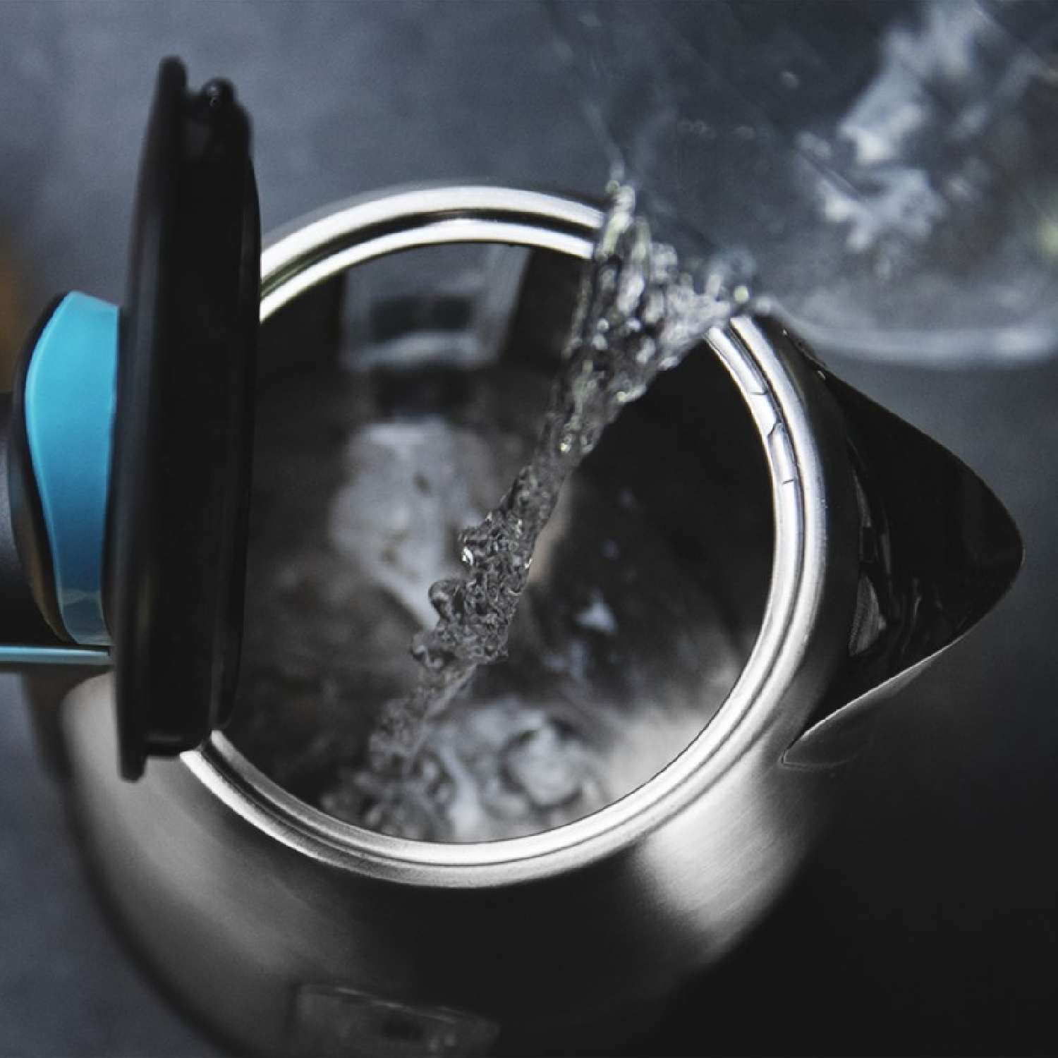 Agua vertiéndose en una tetera. La tetera es plateada con tapa negra y detalles azules.