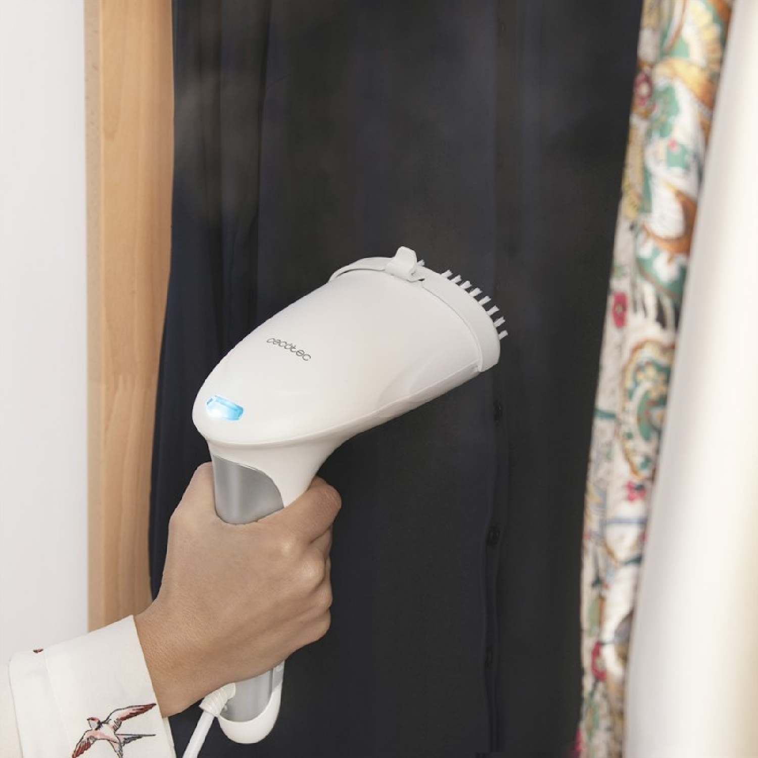 Hand hält weißen Dampfreiniger, der ein schwarzes Kleidungsstück im Schrank bedampft.