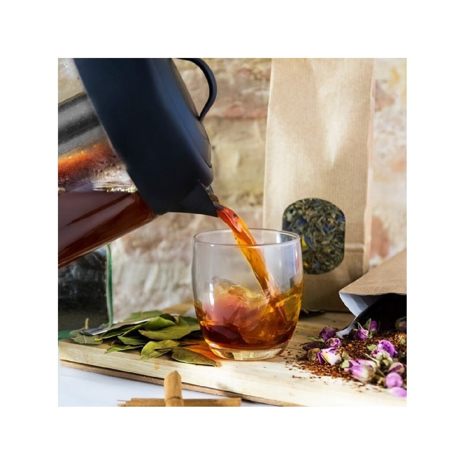 Té vertiéndose en un vaso. Hojas secas, bolsitas de té y flores sobre una superficie de madera.