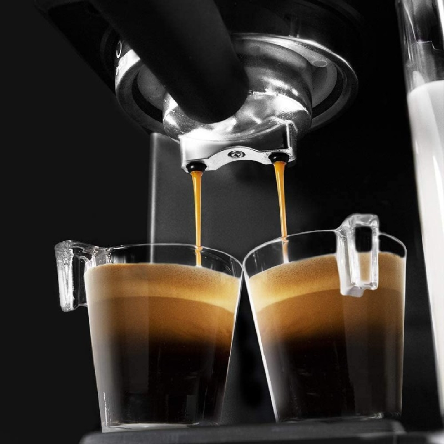 Máquina de espresso que dispensa café en dos tazas transparentes. Las tazas están medio llenas de café.