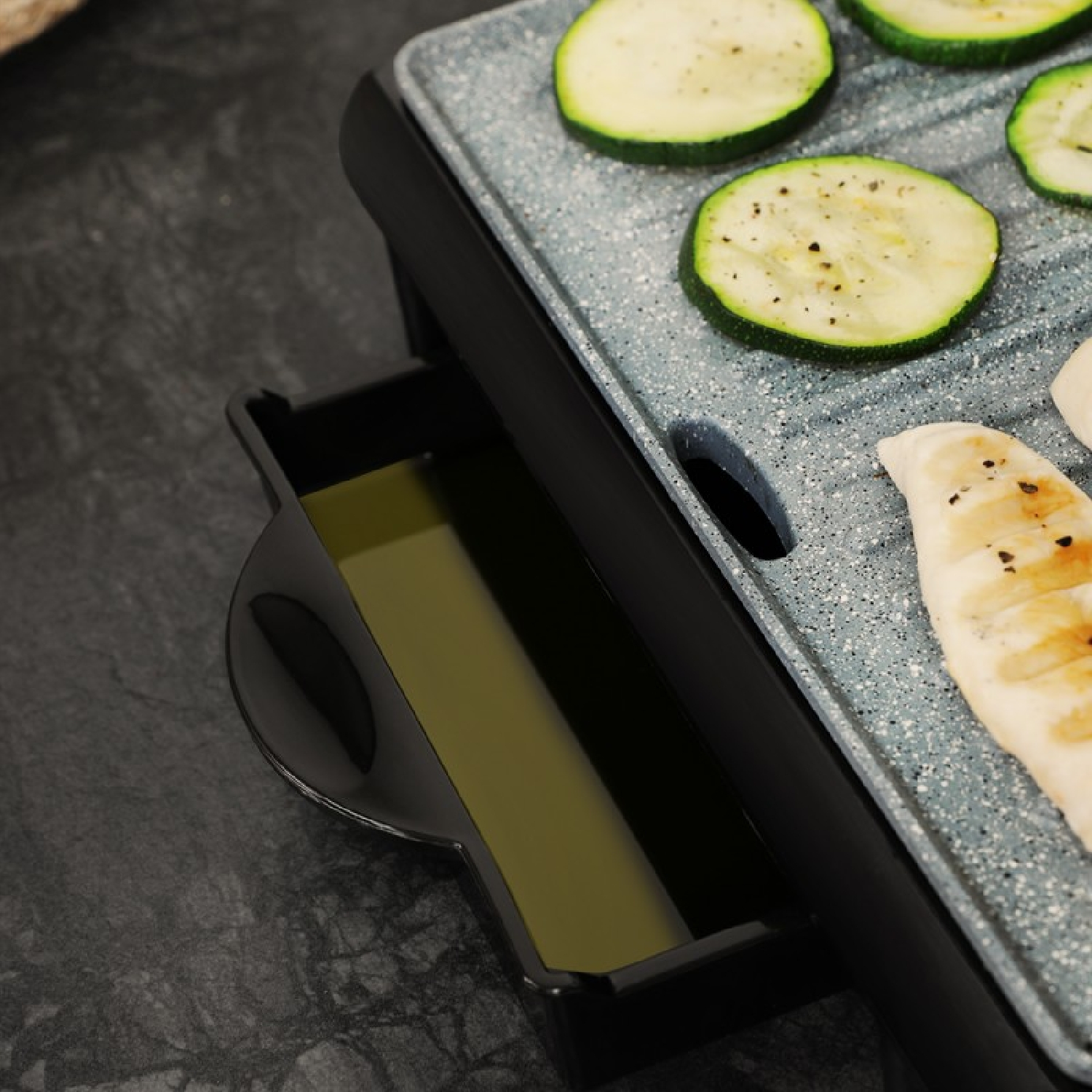 Grill z warzywami i olejem w tacy. Widoczne są plastry cukinii.