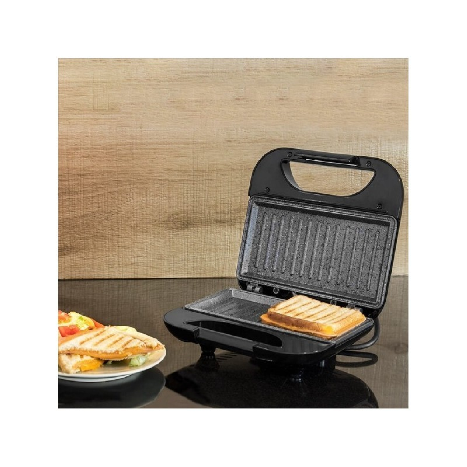 Tostapane nero con sandwich grigliato dentro e un piatto di cibo a sinistra.