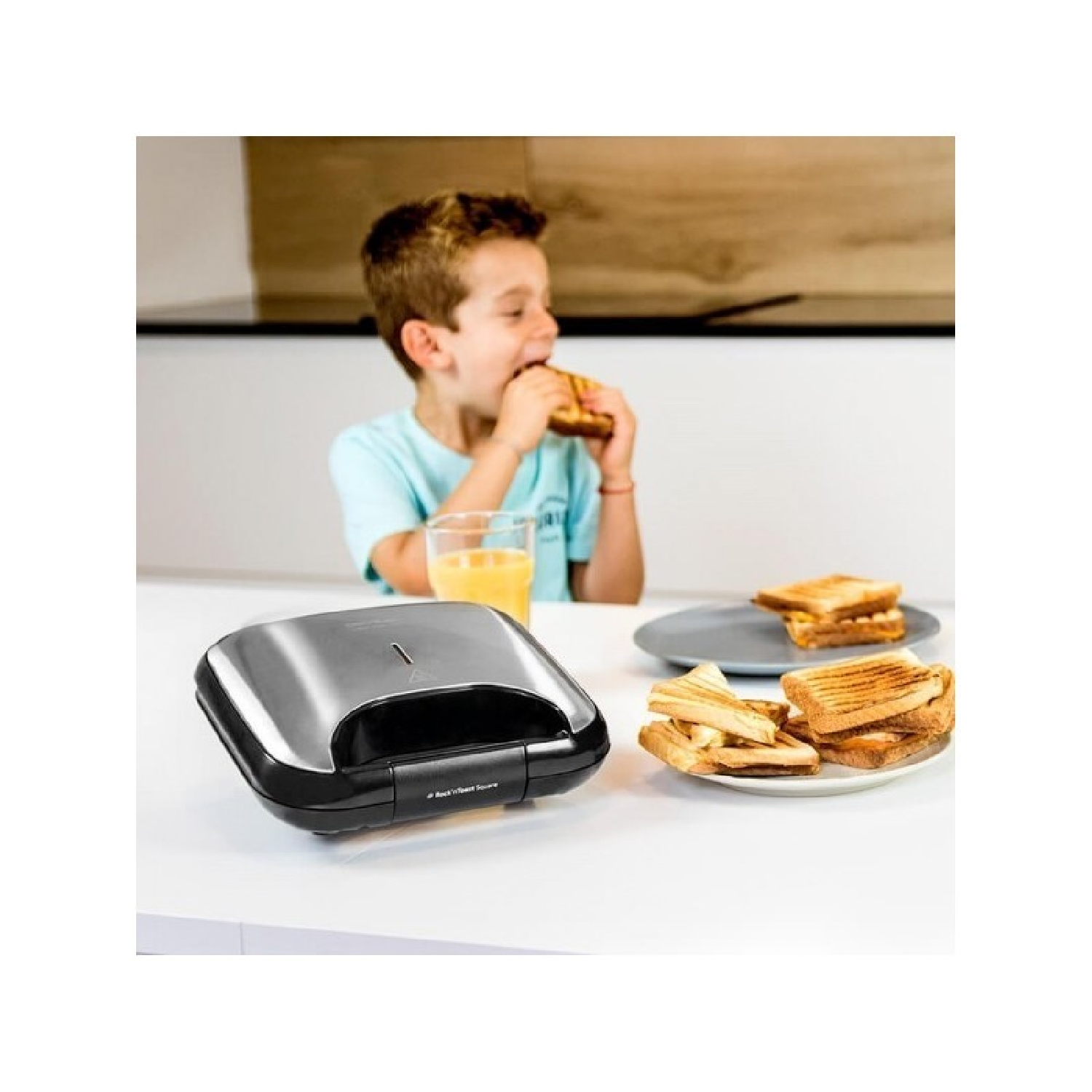 Un ragazzo mangia un panino mentre un'apparecchiatura per panini e panini preparati sono sul tavolo.