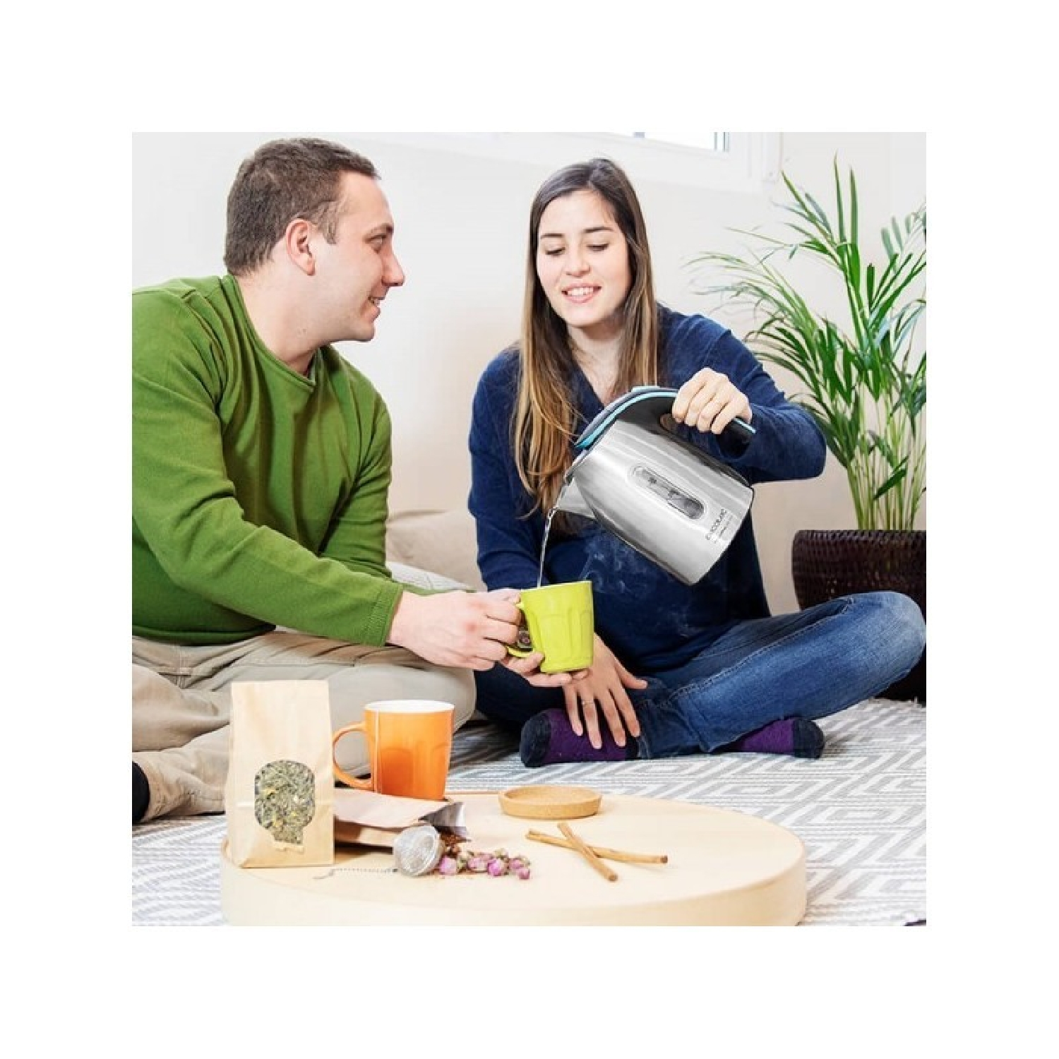 Ein Paar bereitet Tee zu. Auf dem Tisch stehen ein Wasserkocher, eine Tasse und Tee-Zubehör.