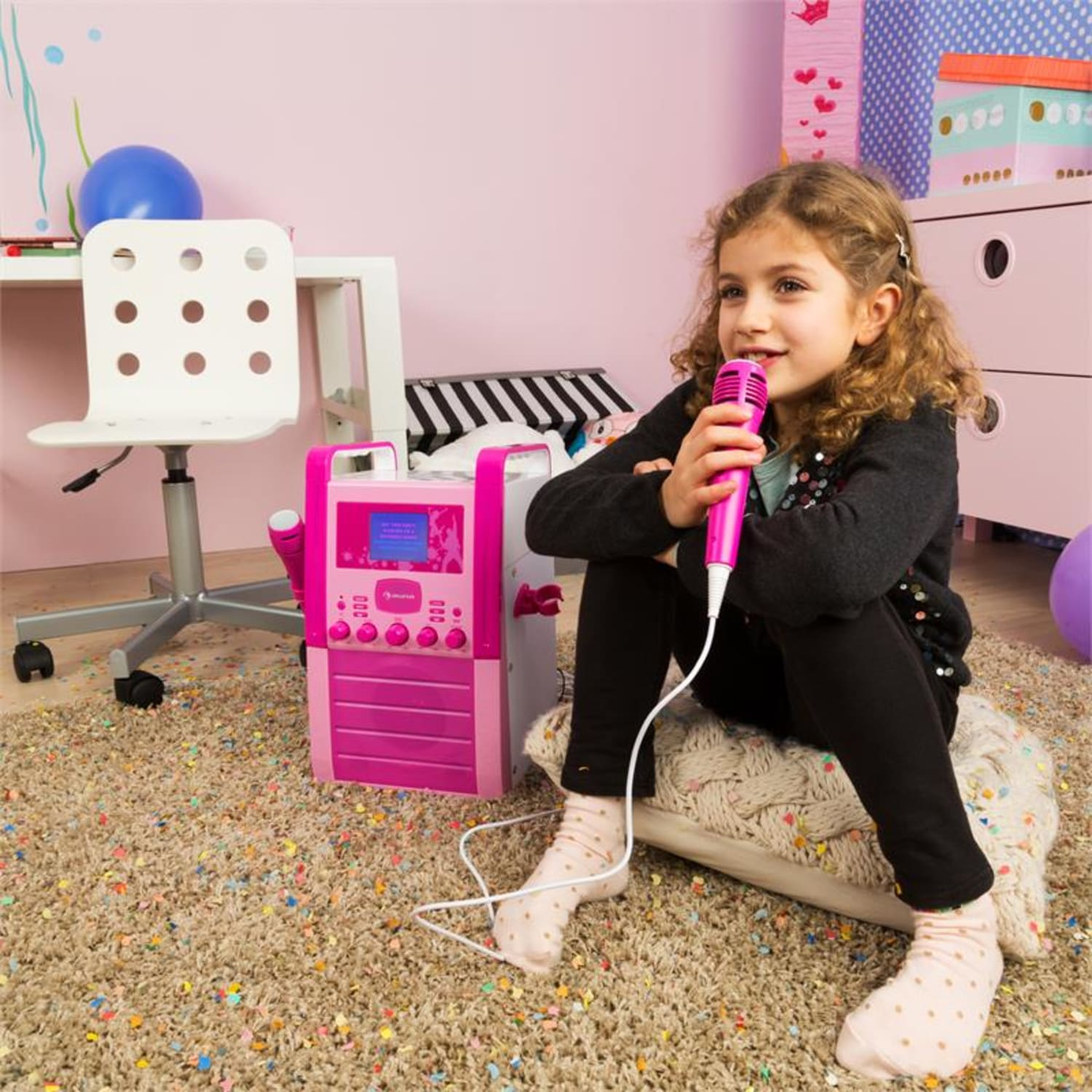 Mädchen singt in pinkes Mikrofon, pinke Karaoke-Maschine, bunter Teppich.