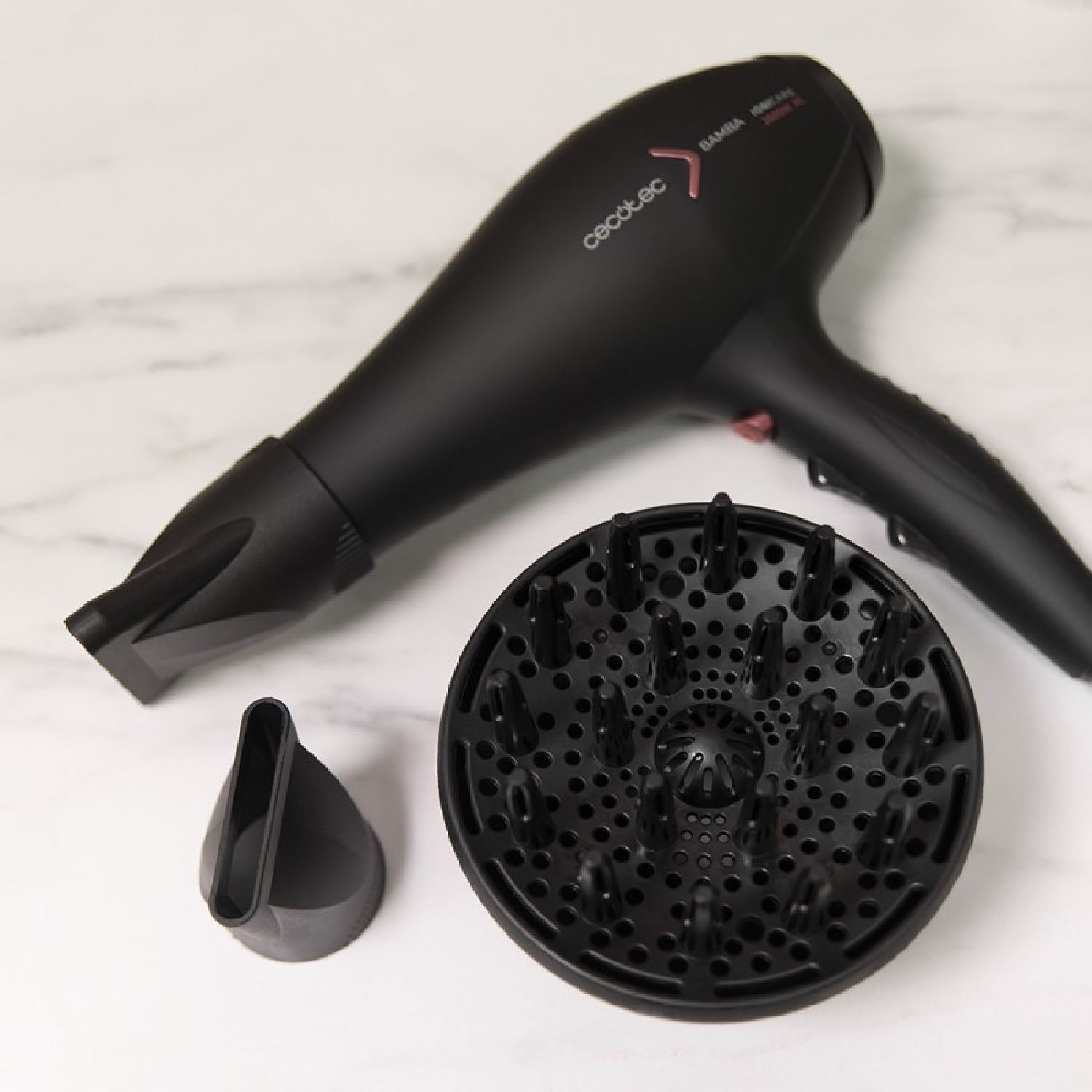 Asciugacapelli nero con accessori, incluso un diffusore, su una superficie di marmo bianco.