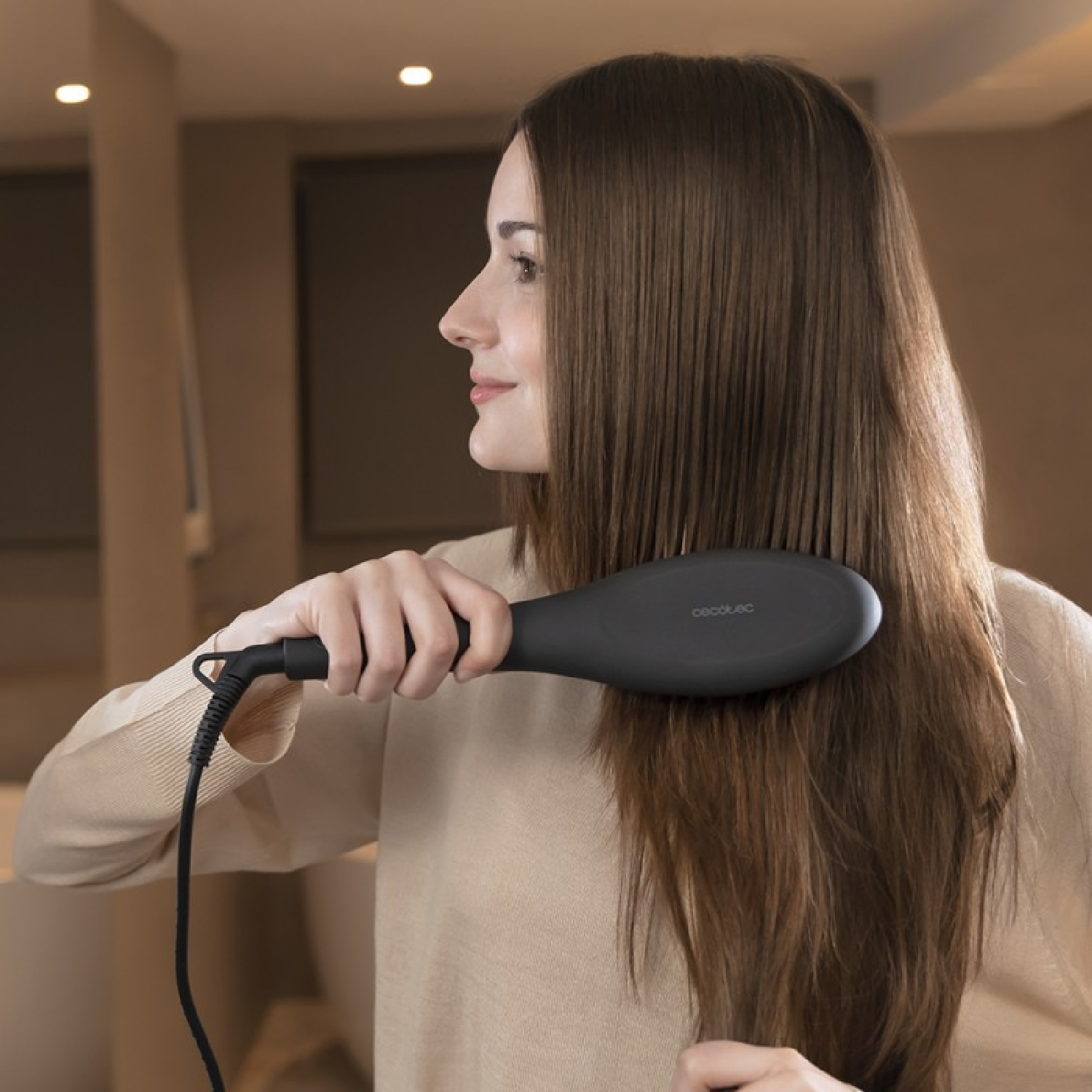 Vrouw die haar haar borstelt met een zwarte haarstijltang. Ze is in een badkamer.
