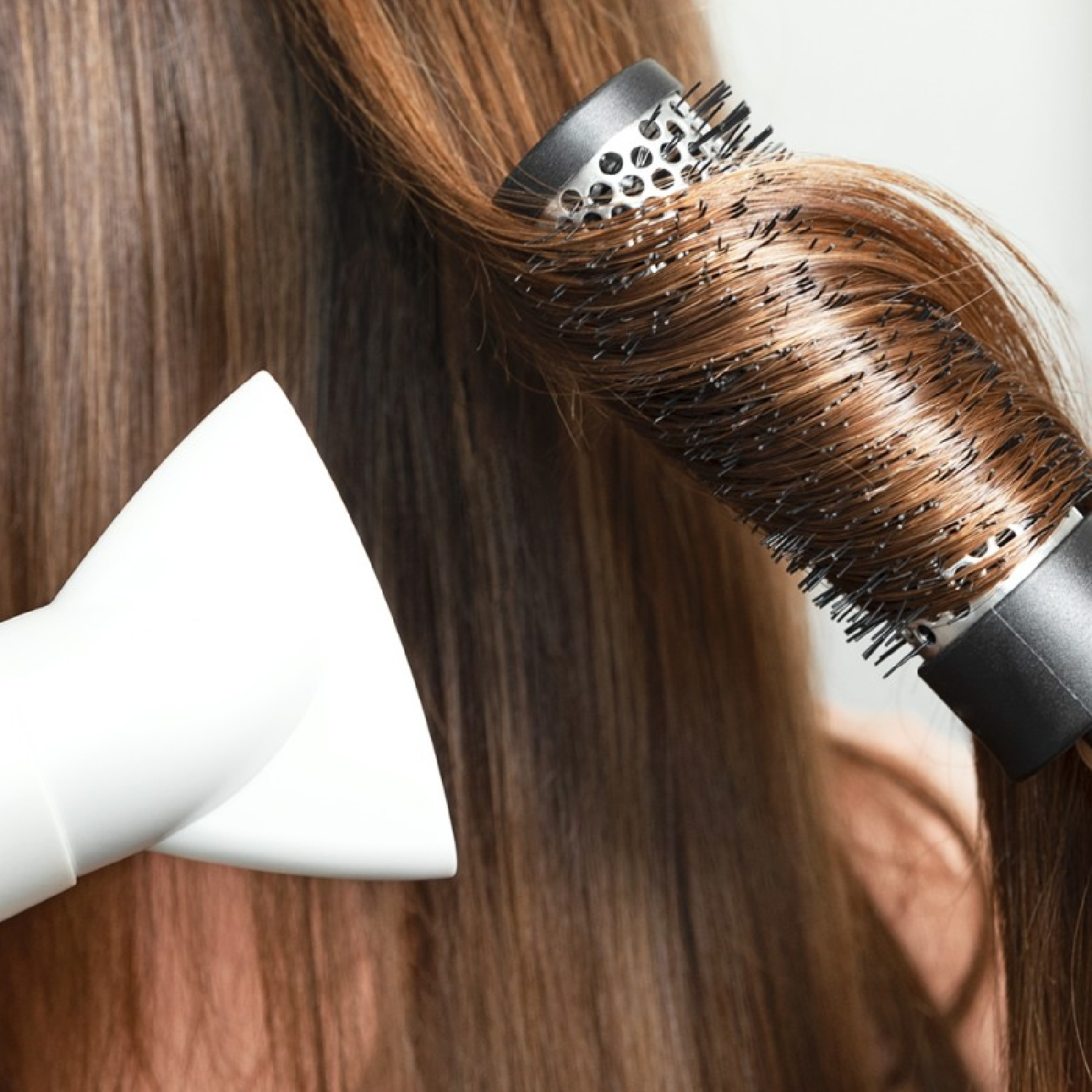Una persona che usa un asciugacapelli e una spazzola rotonda per acconciare i suoi capelli castani.