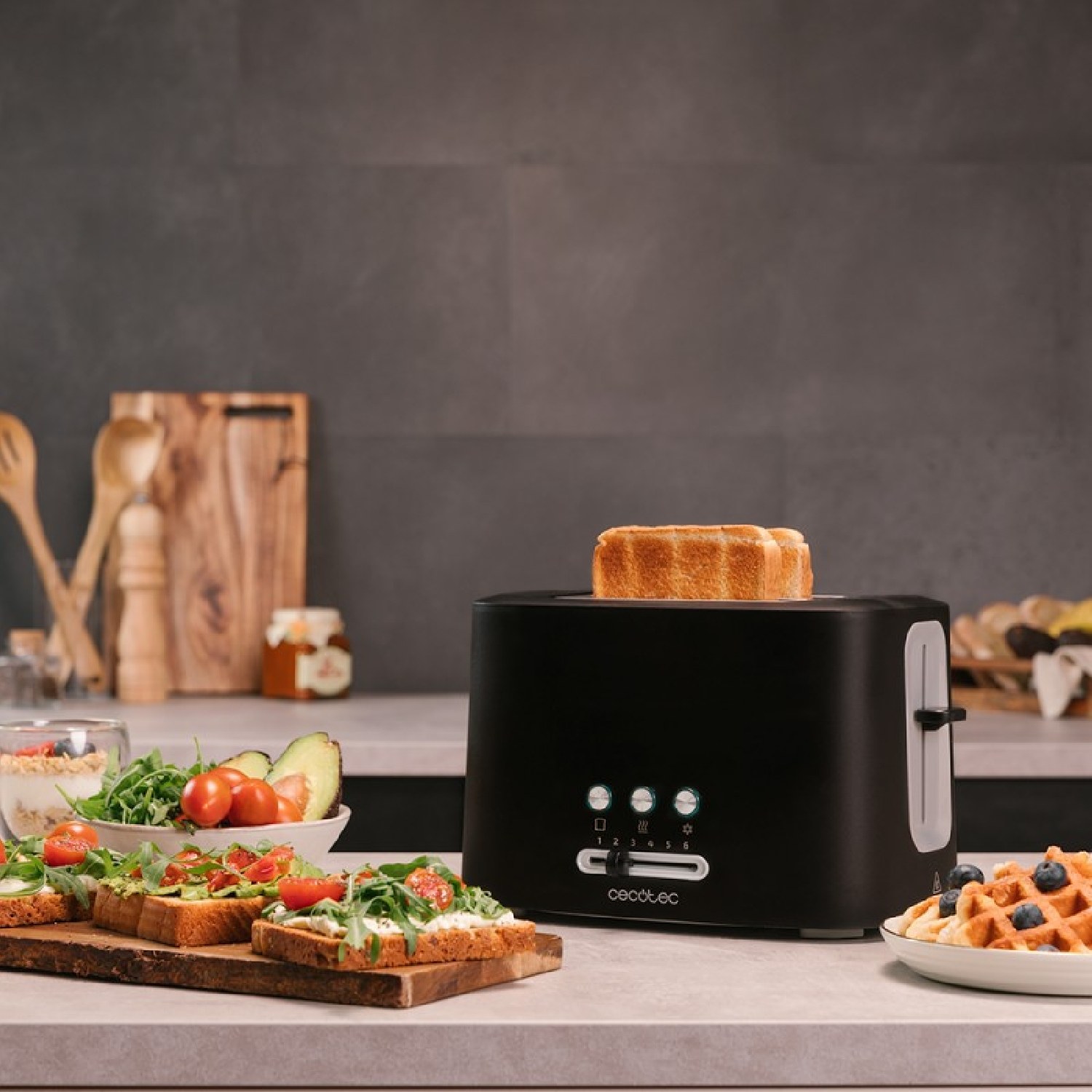A black toaster with toast popping up. Beside is waffles and toast with toppings.