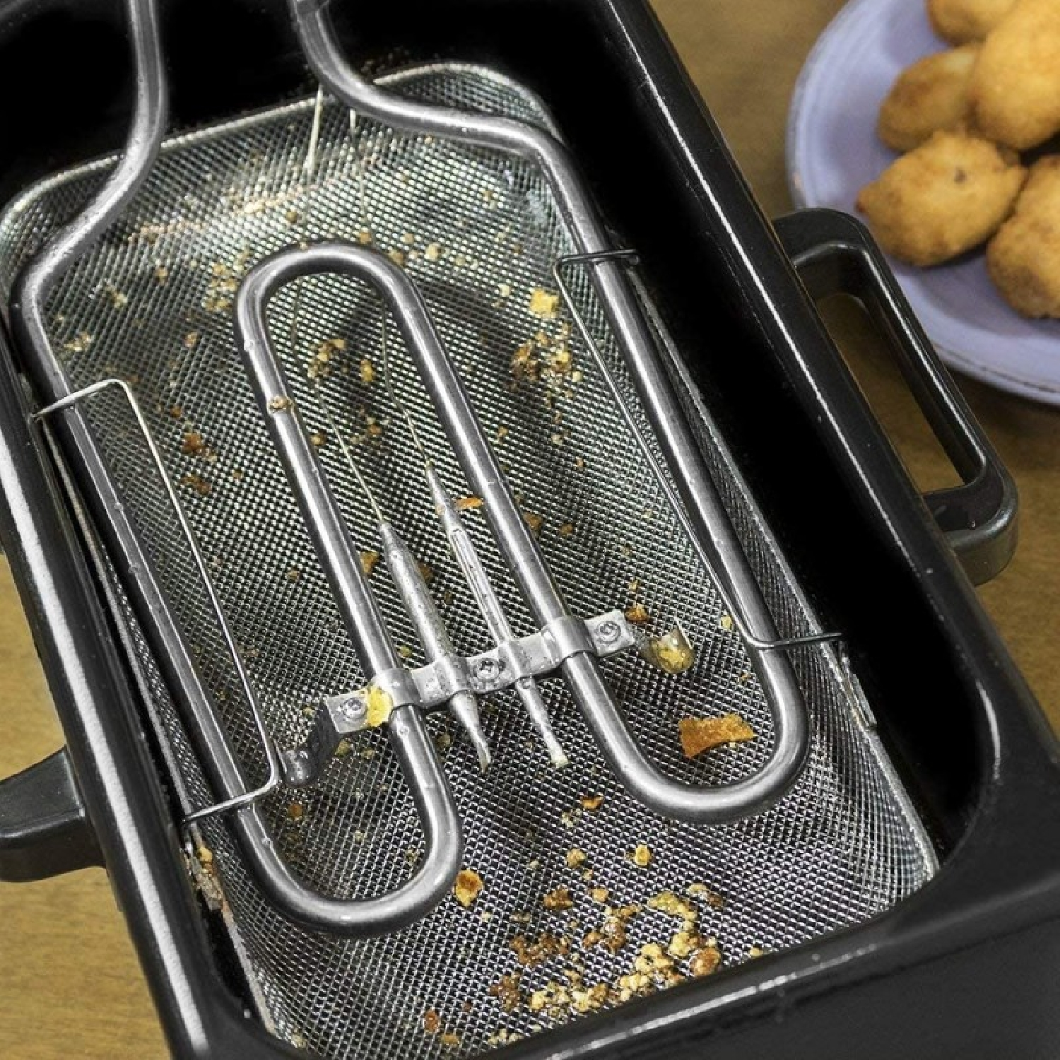 Freidora con un elemento calefactor, restos de comida y una cesta con alimentos fritos.